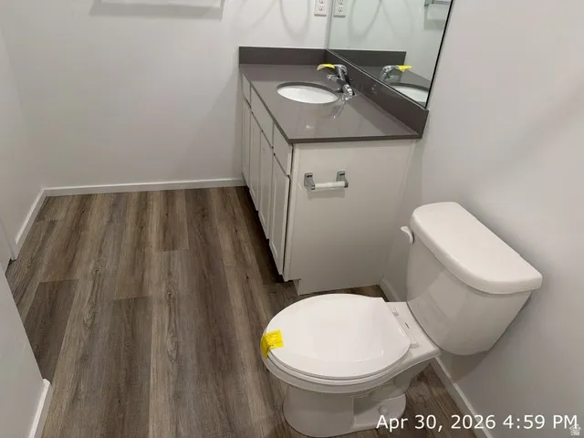 Bathroom featuring wood-finish flooring, a white vanity with shaker-style cabinetry, a gray countertop, and an integrated sink with a chrome faucet