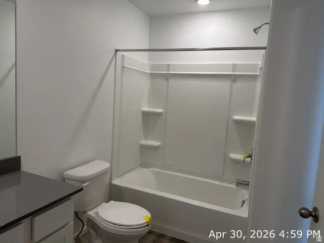 Full bathroom featuring a white tub/shower combination with integrated shelving, a modern toilet, and a vanity with a dark countertop and a large wall mirror