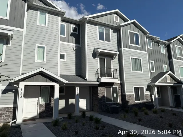 Contemporary townhome exterior featuring light gray siding, dark gray board and batten accents, and a stone-clad foundation