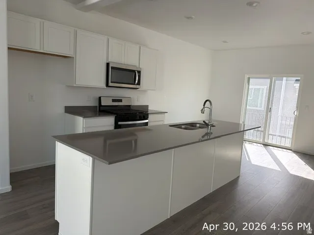 Modern kitchen featuring white cabinetry, dark countertops, wood-finish flooring, a stainless steel gas range, and a spacious island with an integrated sink