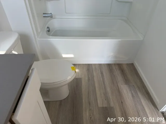 Bathroom featuring a white bathtub, wood-finish flooring, and a toilet