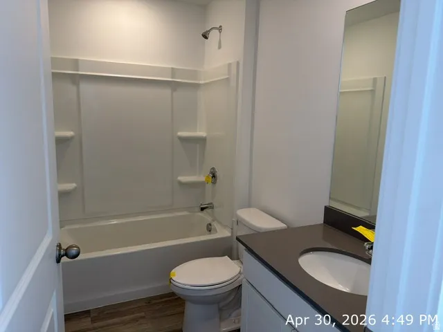 Bathroom featuring a white tub and shower combination with chrome fixtures, a single vanity with a dark countertop and undermount sink, a large wall-mounted mirror, and wood-finish flooring