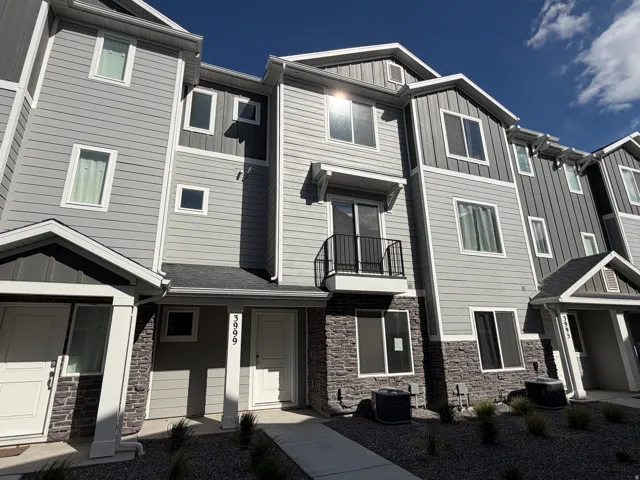 Multi-story townhome exterior featuring stone veneer accents, horizontal and vertical siding, white trim, a private balcony with a black railing, and multiple windows