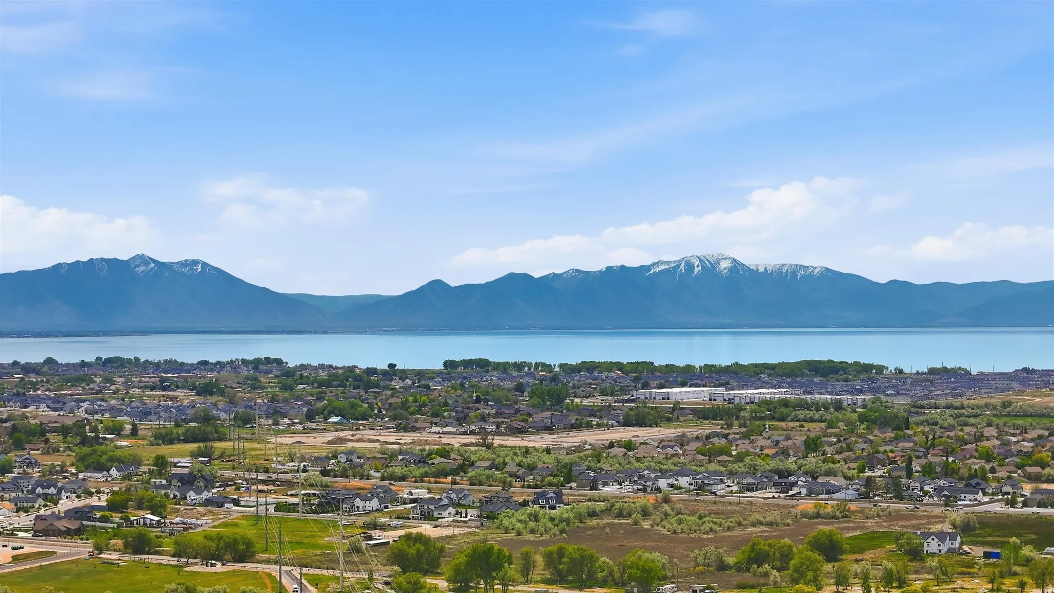 Expansive aerial perspective showcasing a significant body of water bordered by snow-capped mountains and a residential community