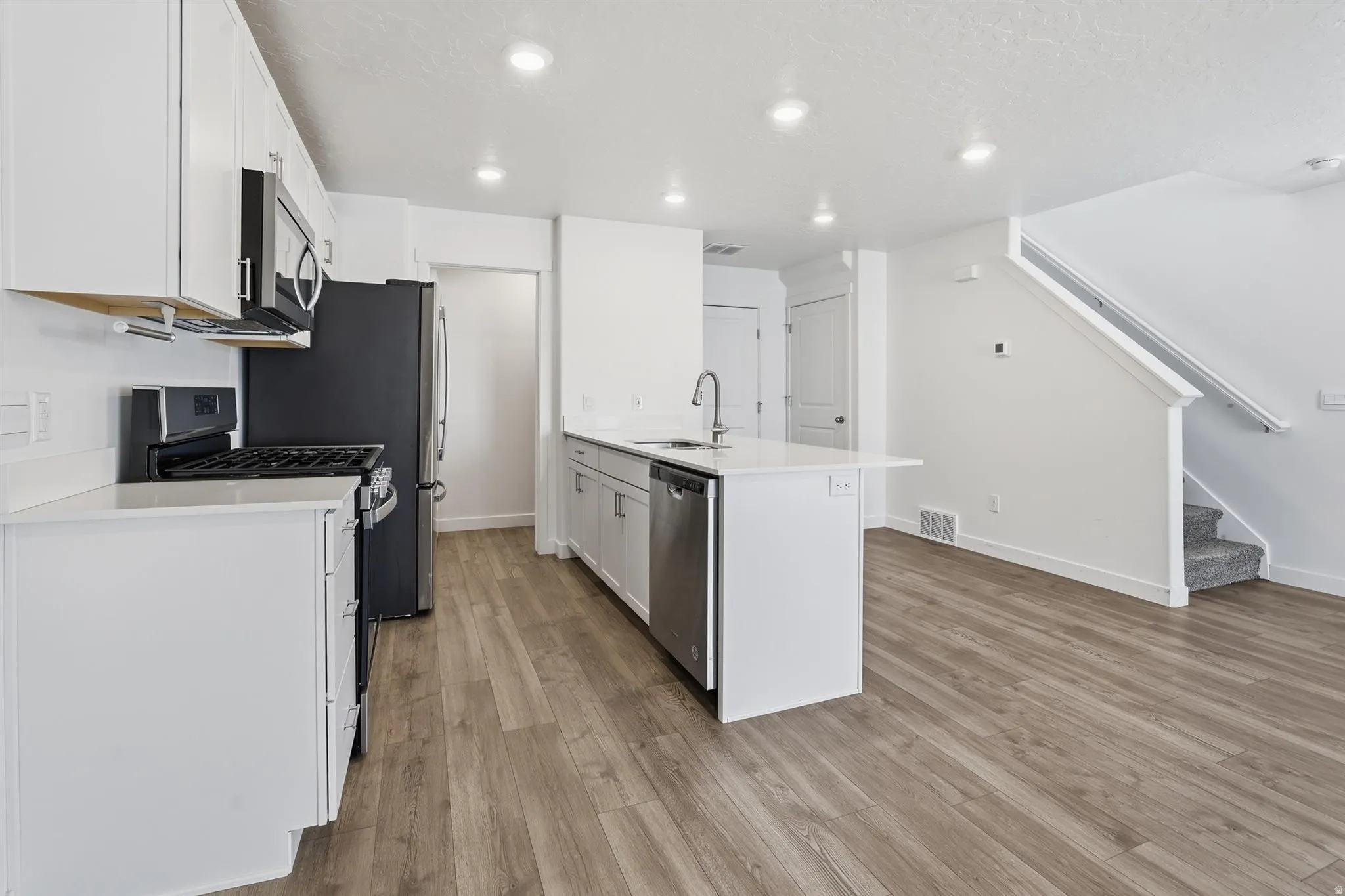Modern kitchen featuring white cabinetry, stainless steel appliances, a center island with a sink, and wood-finish flooring
