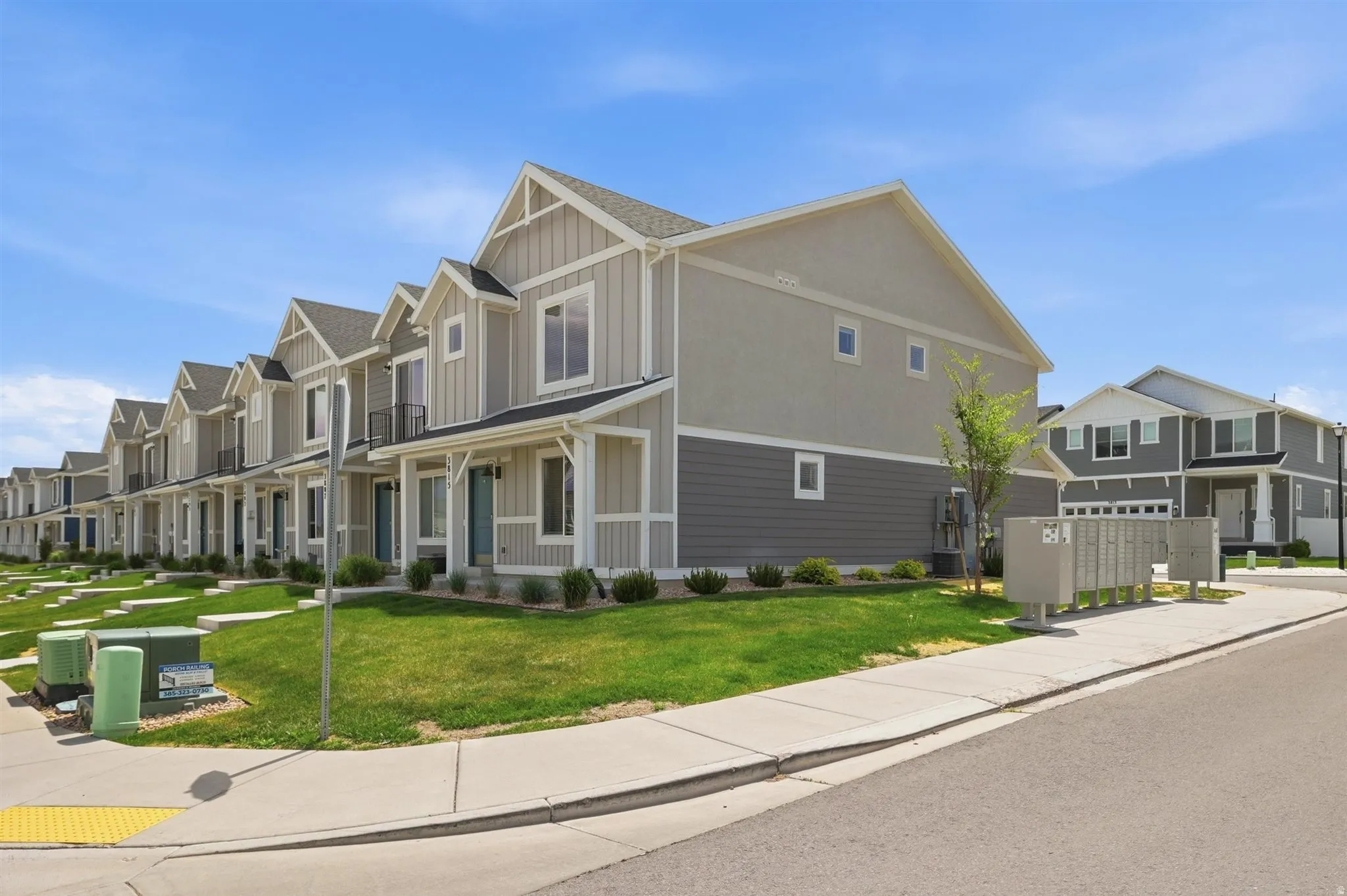 Contemporary townhome-style residences featuring board and batten siding, gabled rooflines, covered front porches, and a landscaped yard