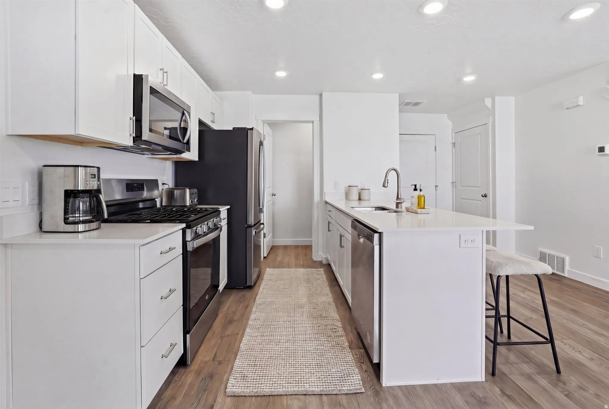Contemporary kitchen featuring white cabinetry, stainless steel appliances, light wood-finish flooring, recessed lighting, and an island with a breakfast bar