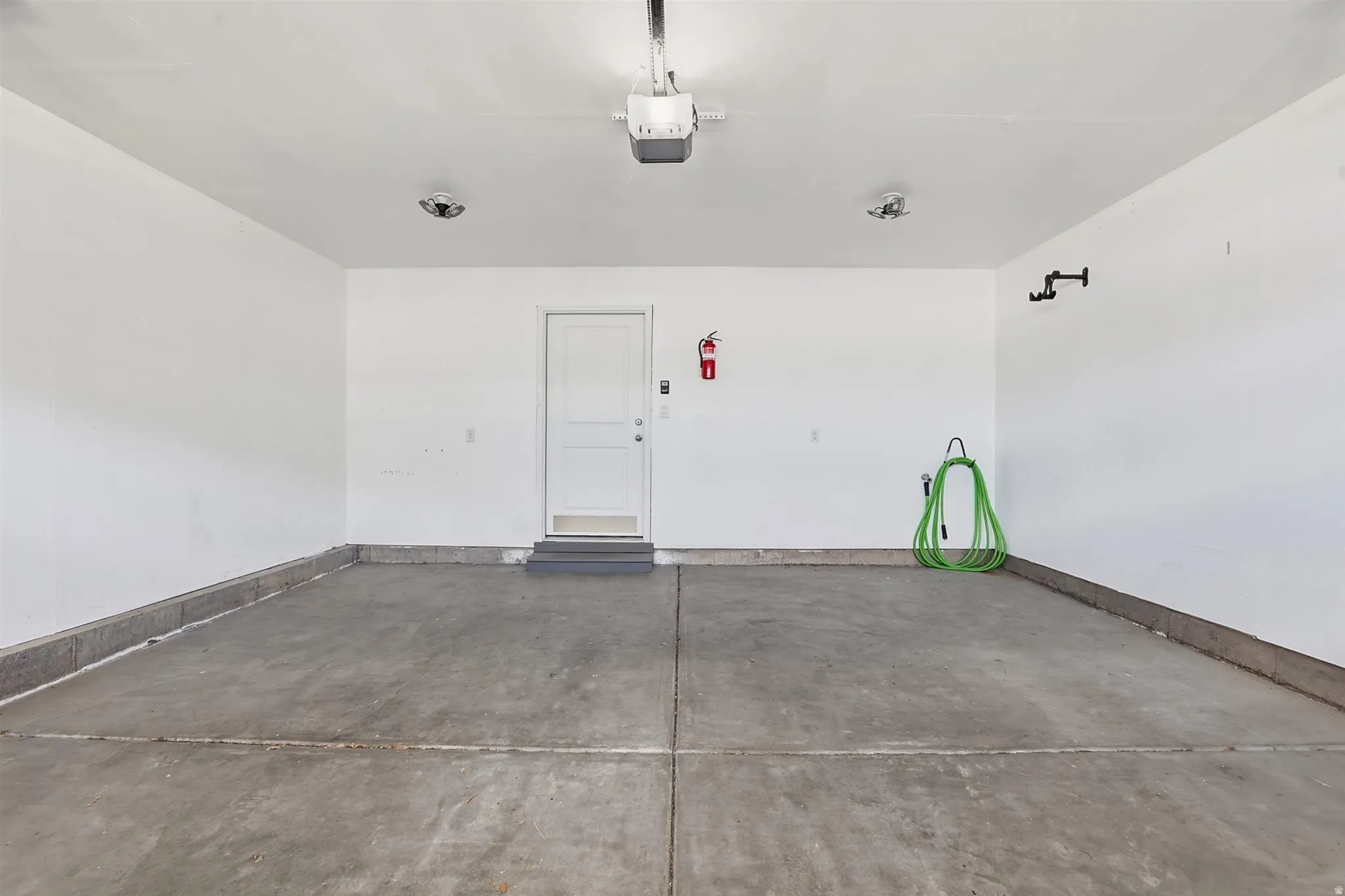 Concrete flooring garage featuring a white door, overhead garage door opener, and interior lighting