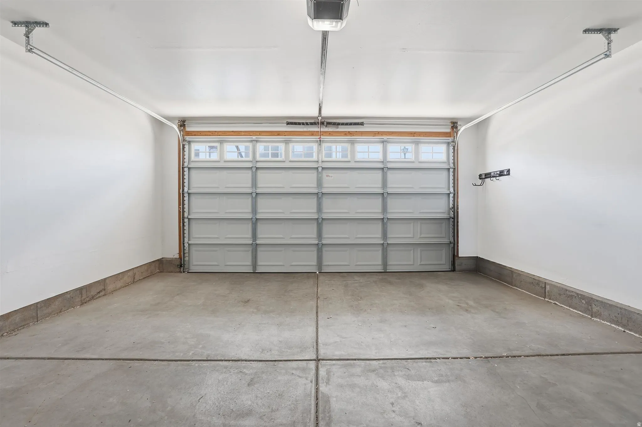 Spacious garage featuring a concrete floor, bright white walls, overhead lighting, and a paneled garage door with upper window inserts