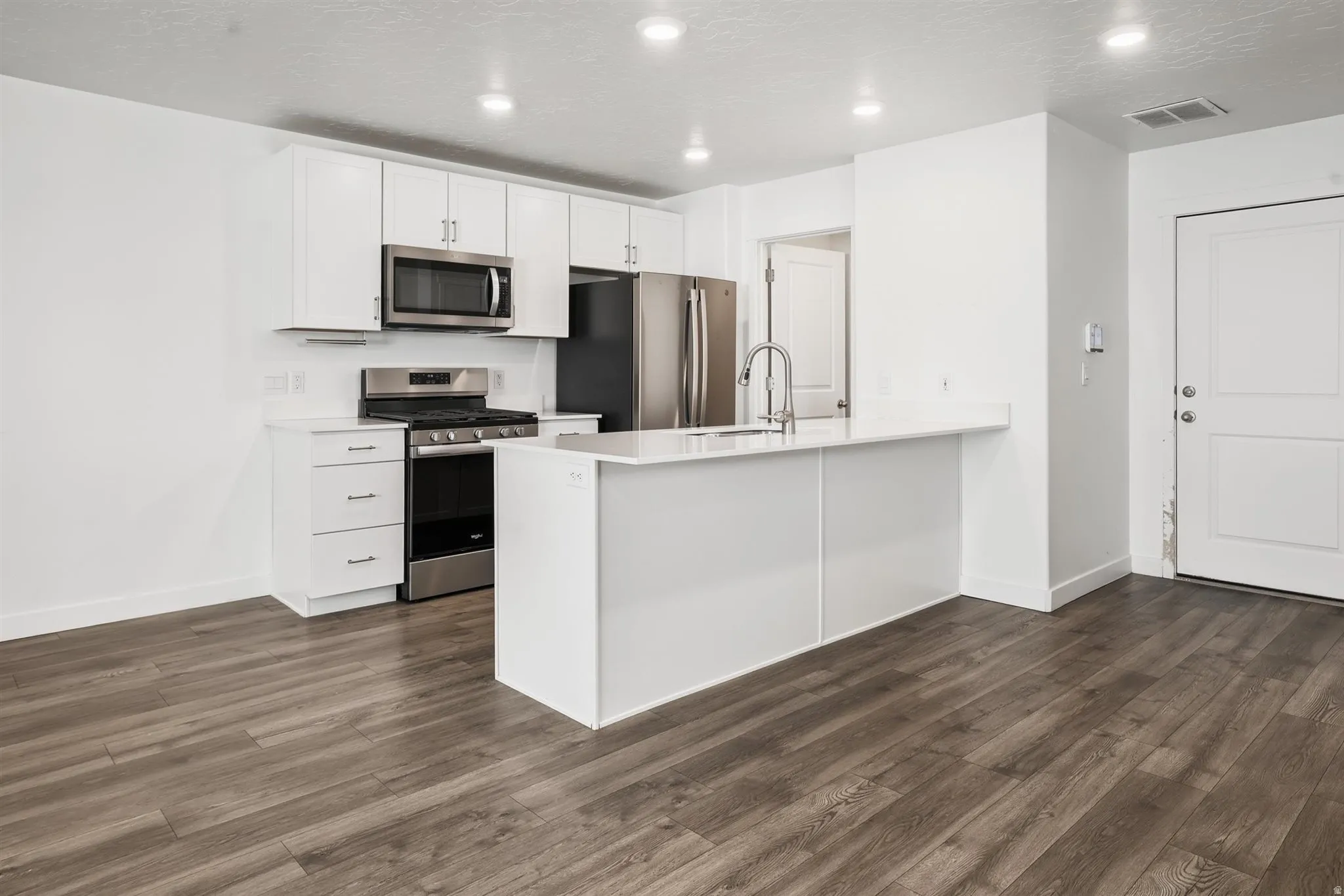 Open-concept kitchen featuring white cabinetry, stainless steel appliances, a kitchen island with seating space, and wood-finish flooring