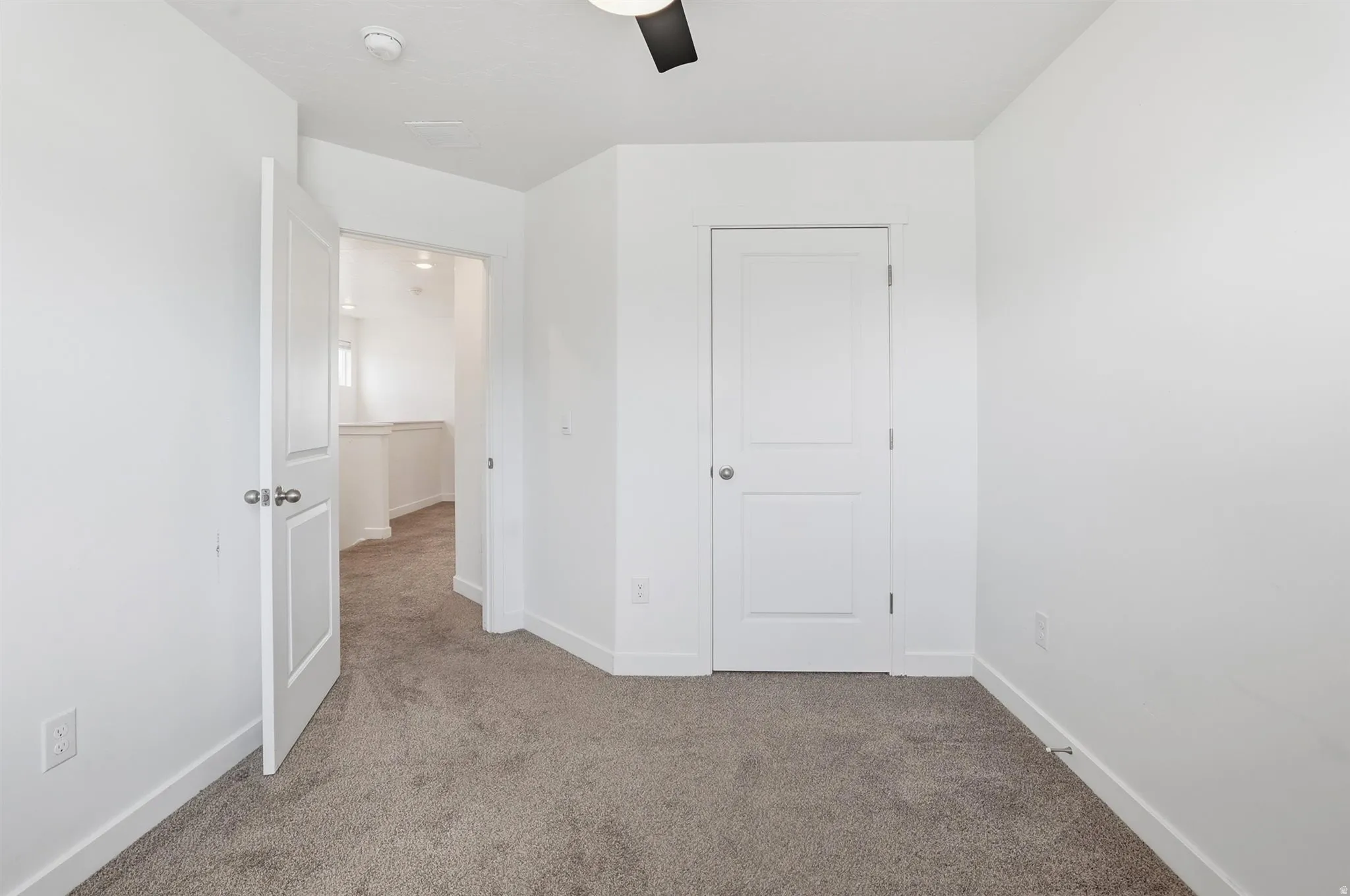 Carpeted room featuring a white ceiling fan, white paneled doors, and white baseboards