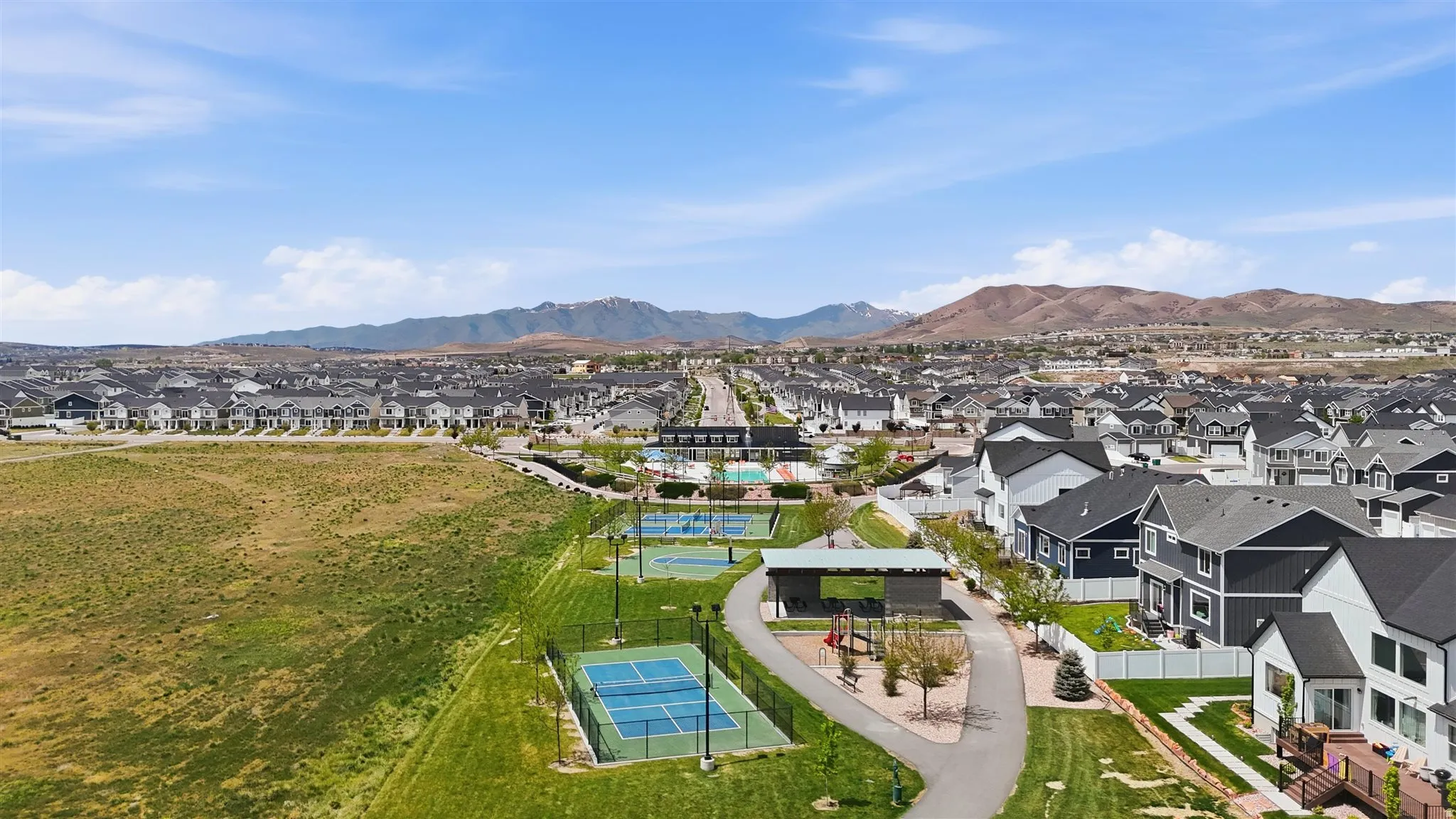 Aerial perspective showcasing a residential community with contemporary homes, two tennis courts, and a playground area with a covered structure