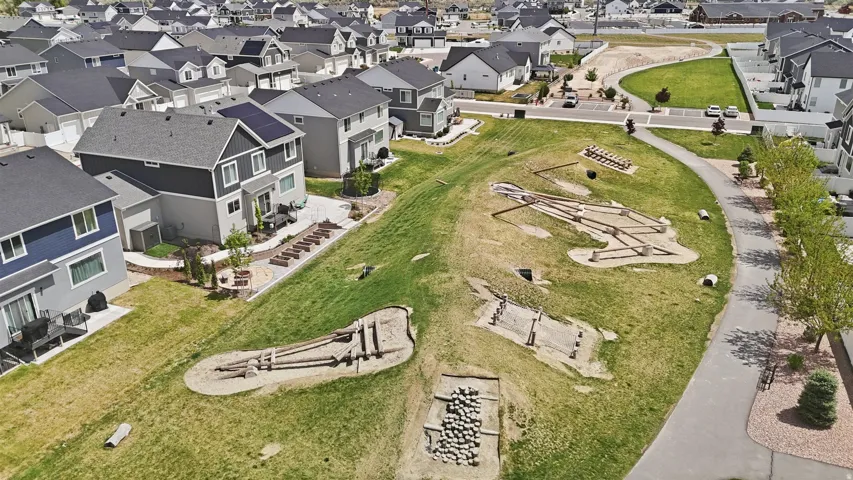 Expansive green space featuring multiple natural play structures, a paved walking path, and mature trees