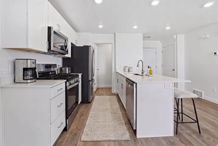 Contemporary kitchen featuring white cabinetry, stainless steel appliances, light wood-finish flooring, recessed lighting, and an island with a breakfast bar