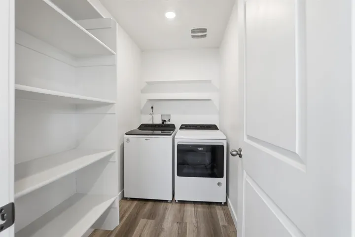 Dedicated laundry area with wood-finish flooring, featuring a top-load washer and front-load dryer