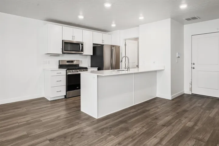 Open-concept kitchen featuring white cabinetry, stainless steel appliances, a kitchen island with seating space, and wood-finish flooring