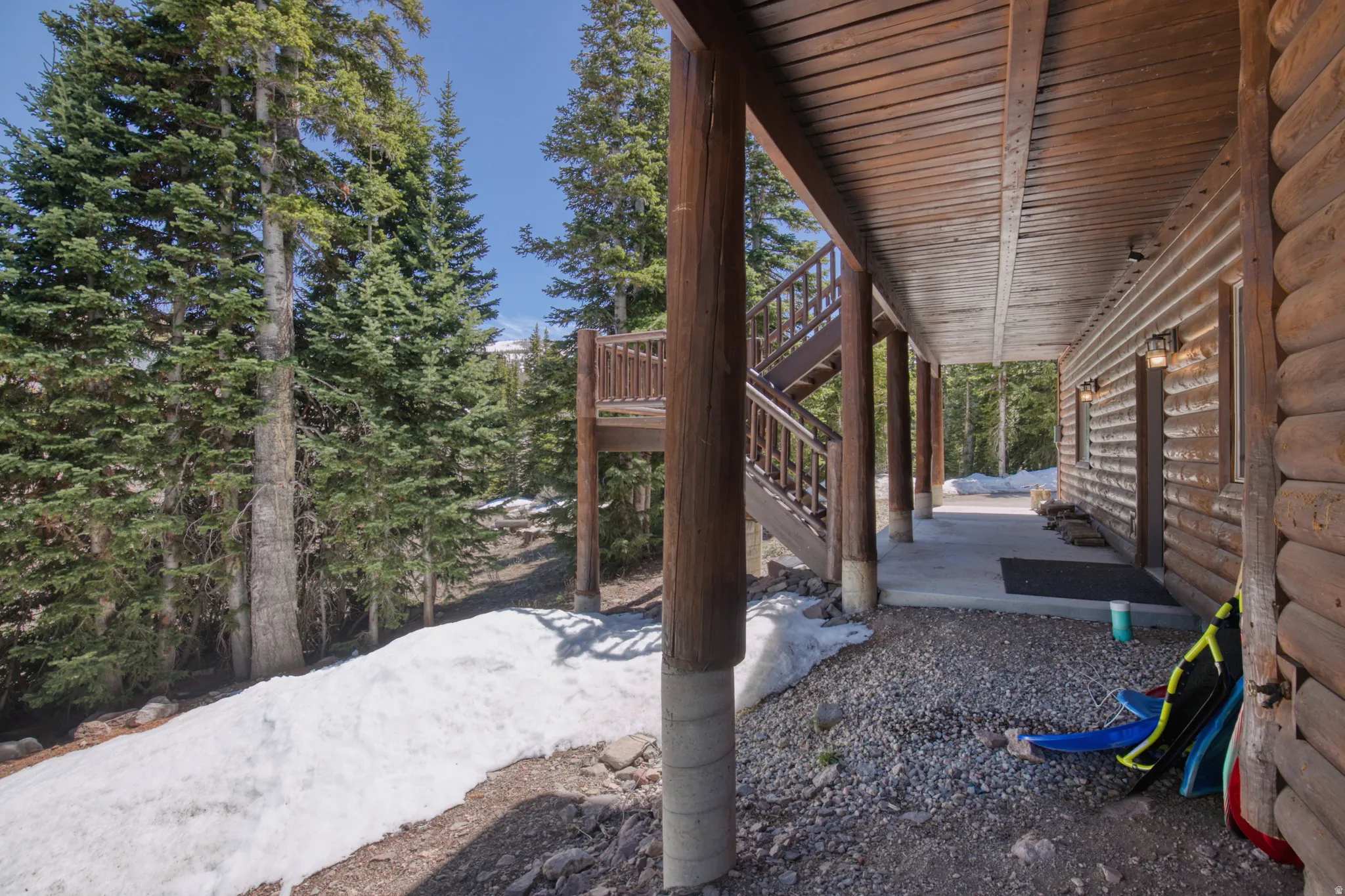 Exterior log cabin siding with an expansive covered porch, featuring a wood-plank ceiling and exposed support beams