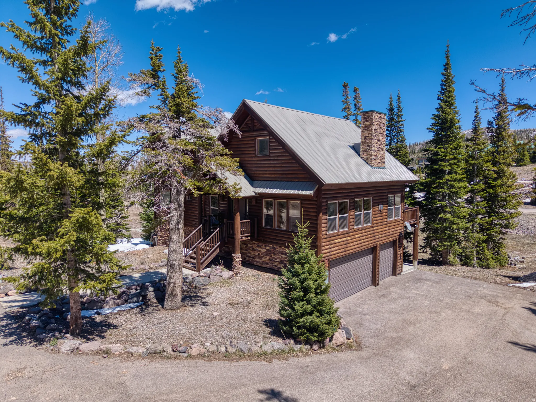 Log cabin structure featuring a metal roof, prominent stone chimney, and a multi-level design