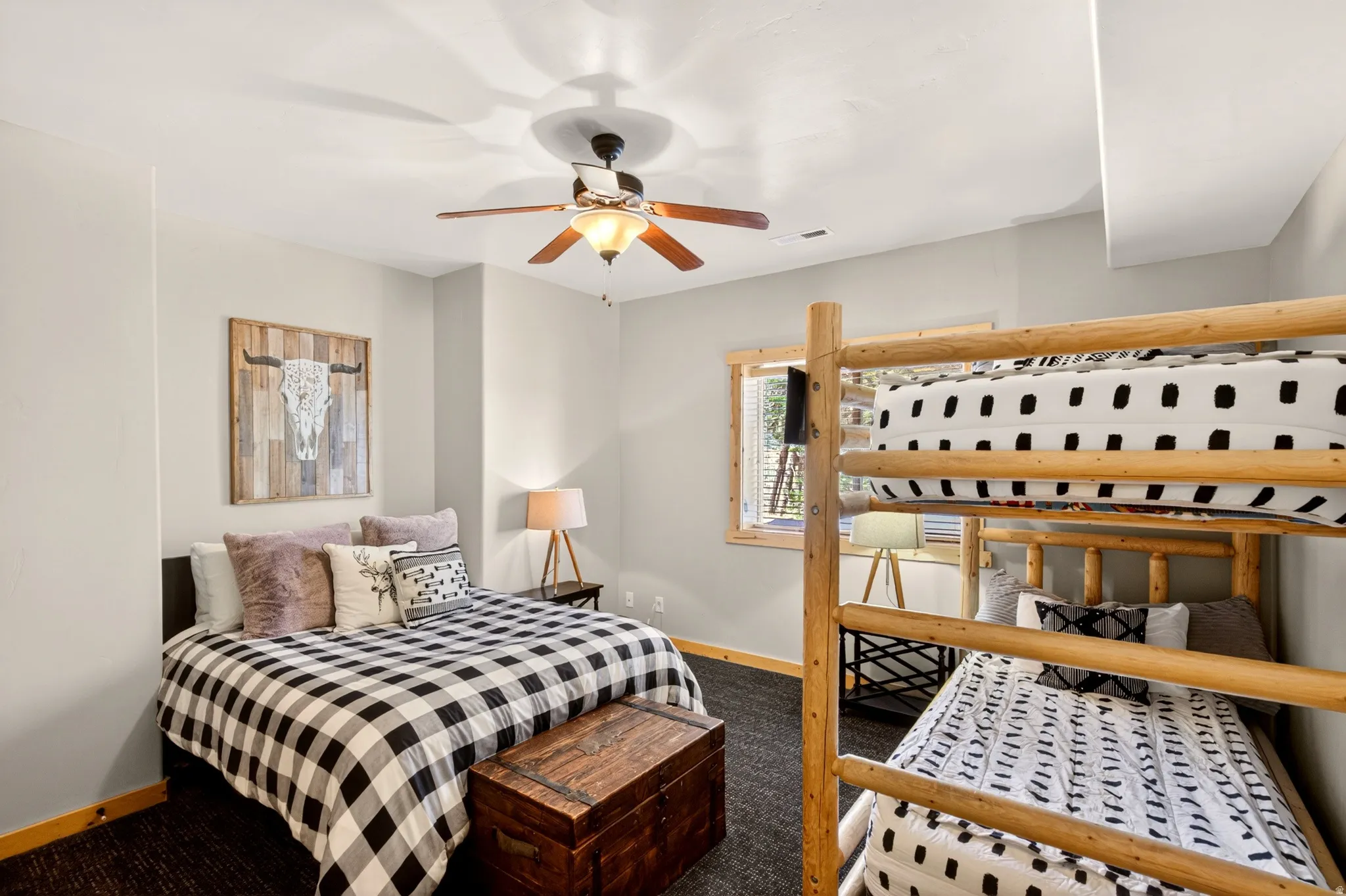 Bedroom featuring a full-size bed, a natural wood bunk bed, a ceiling fan with integrated lighting, wood-finish flooring, and a window with wood trim