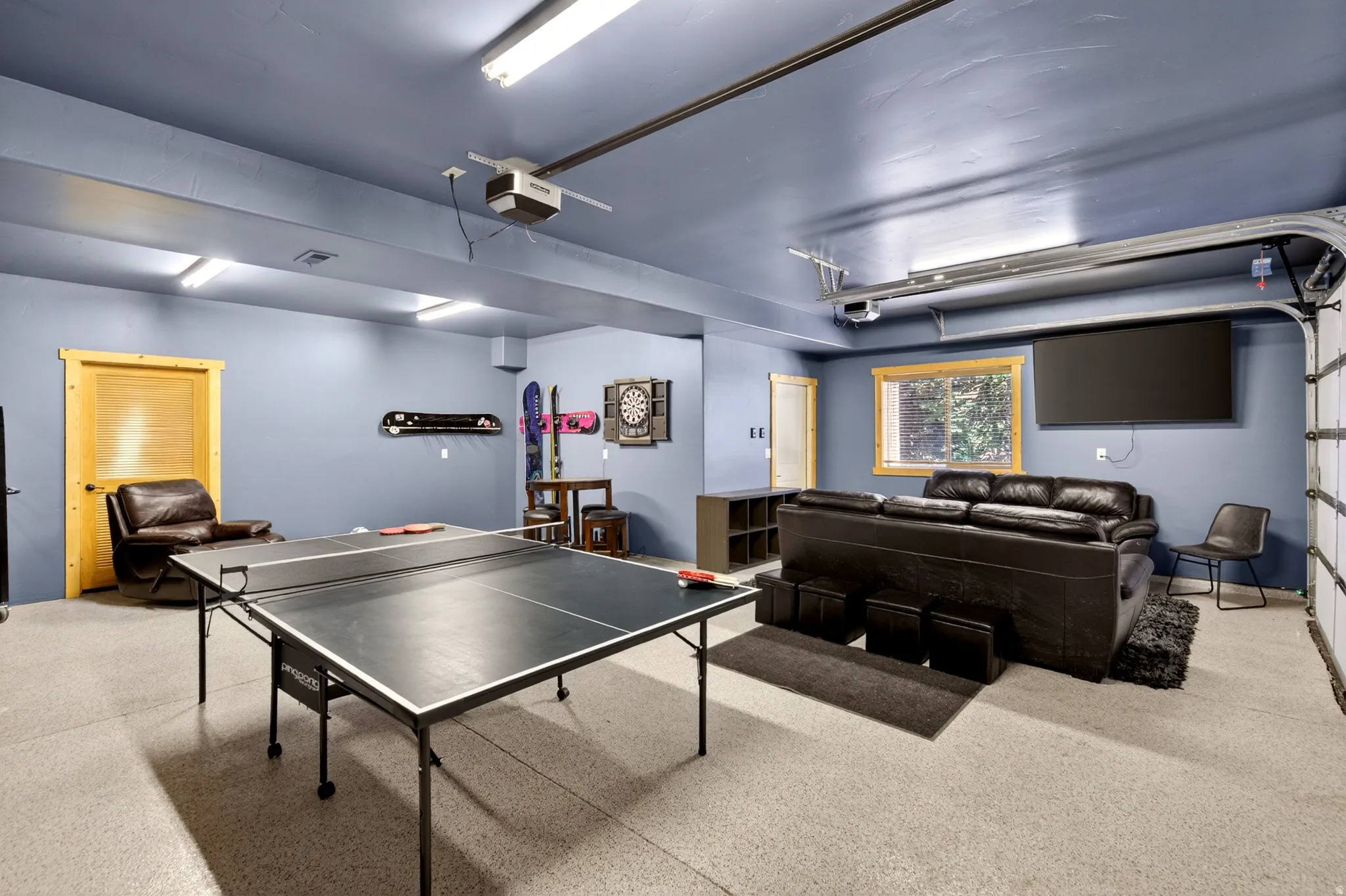 Spacious multi-purpose room featuring a light-colored epoxy floor, recessed lighting, and a large window with natural wood trim