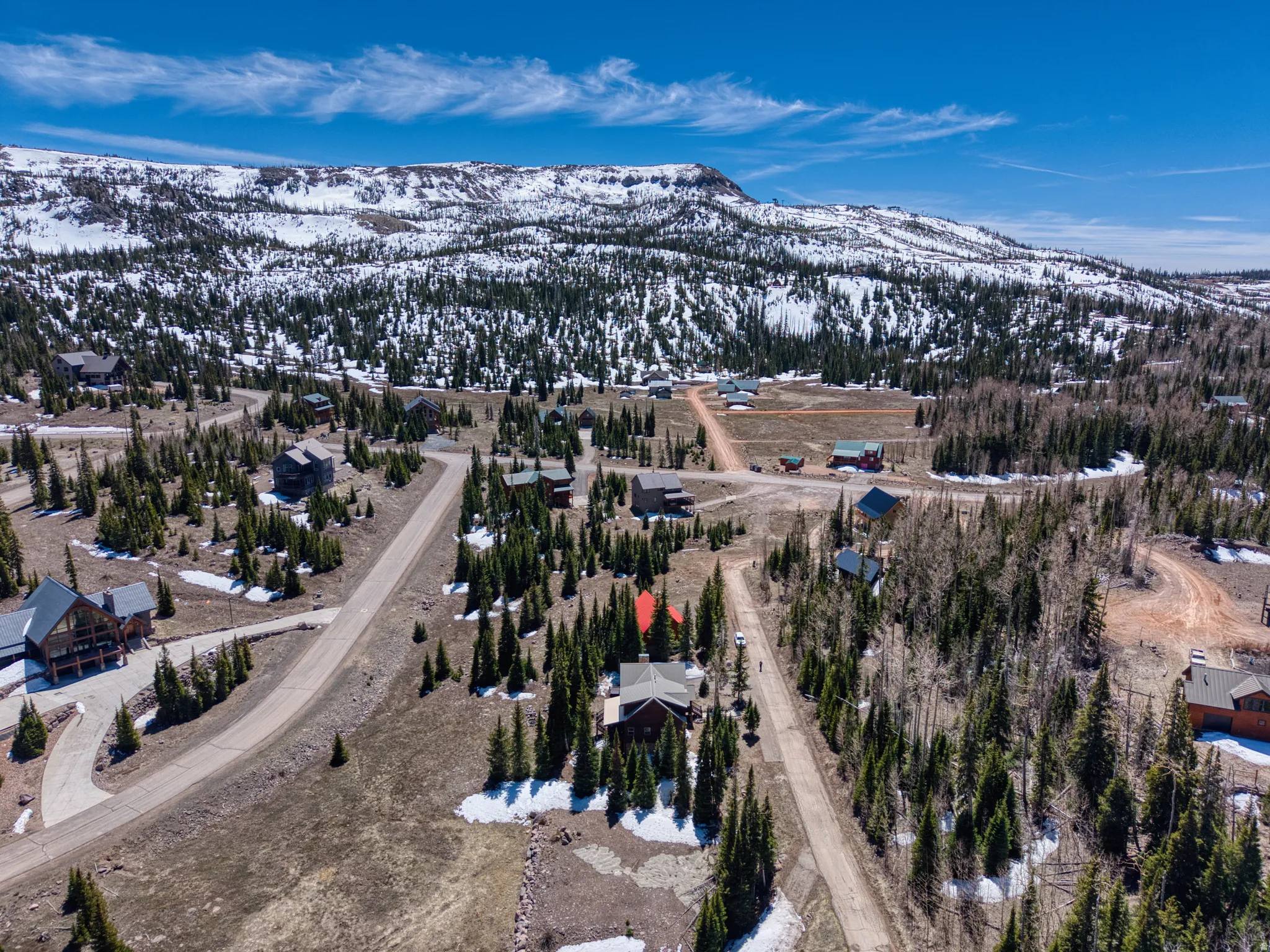 Mountainous landscape with sparse evergreen and deciduous trees, featuring scattered residential properties with varying architectural styles