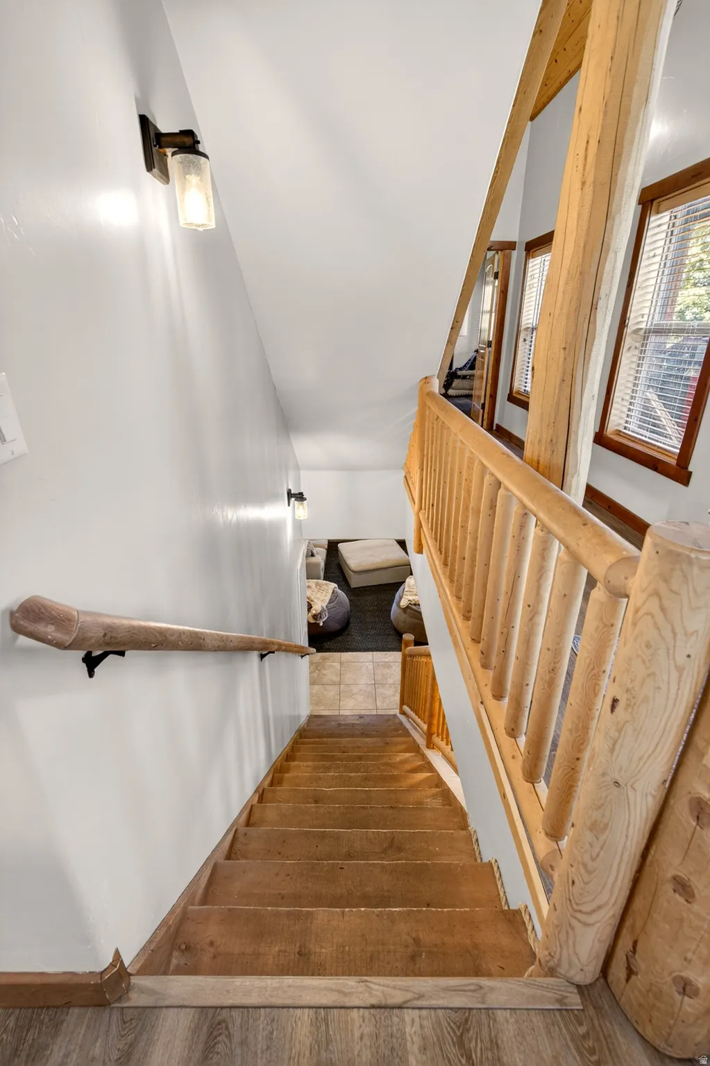 Wood-finish staircase with rustic log railing and handrail, illuminated by wall-mounted sconces