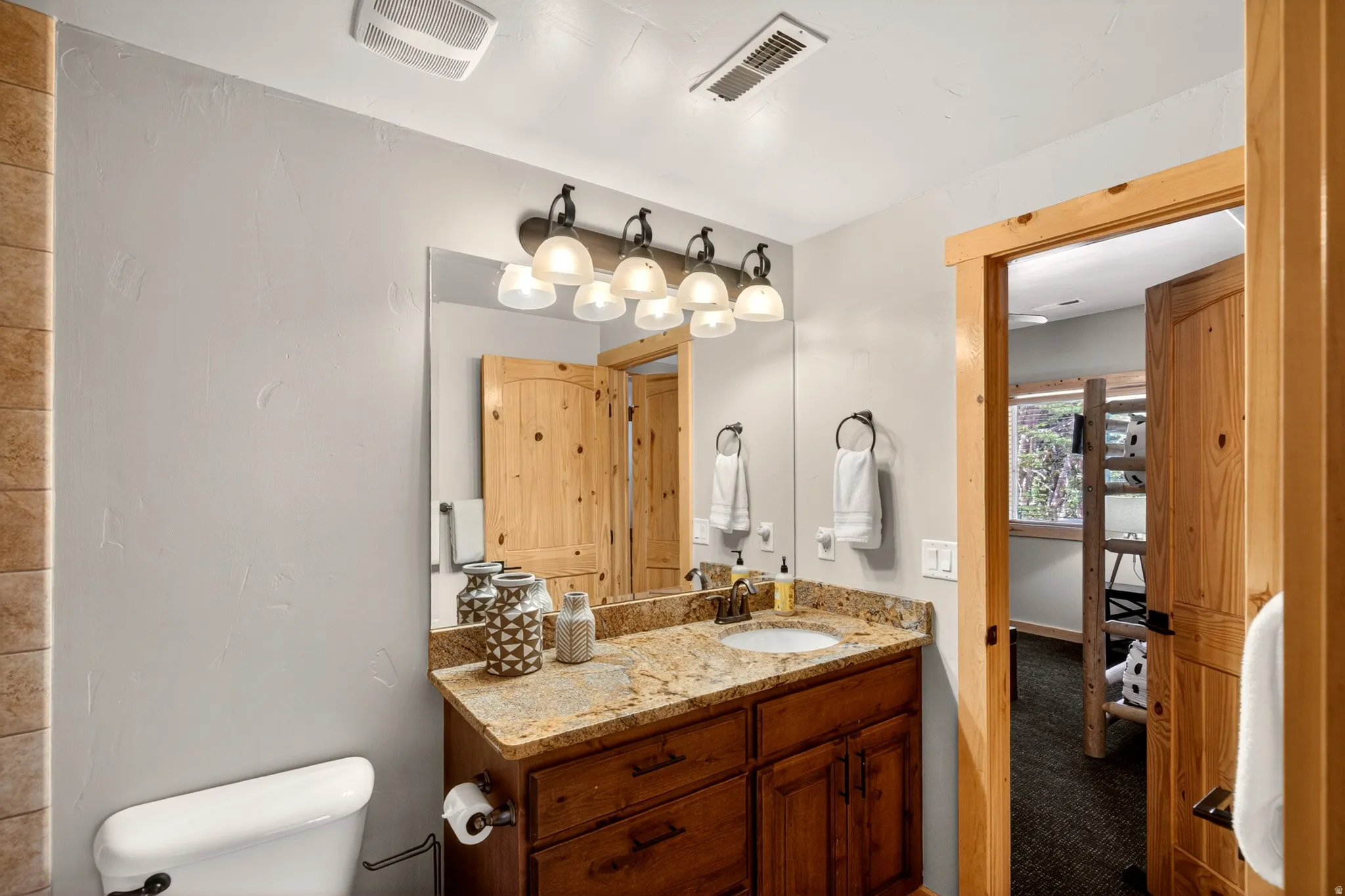 Bathroom featuring a dark wood vanity with a light-colored stone countertop, an undermount sink, and a four-light fixture