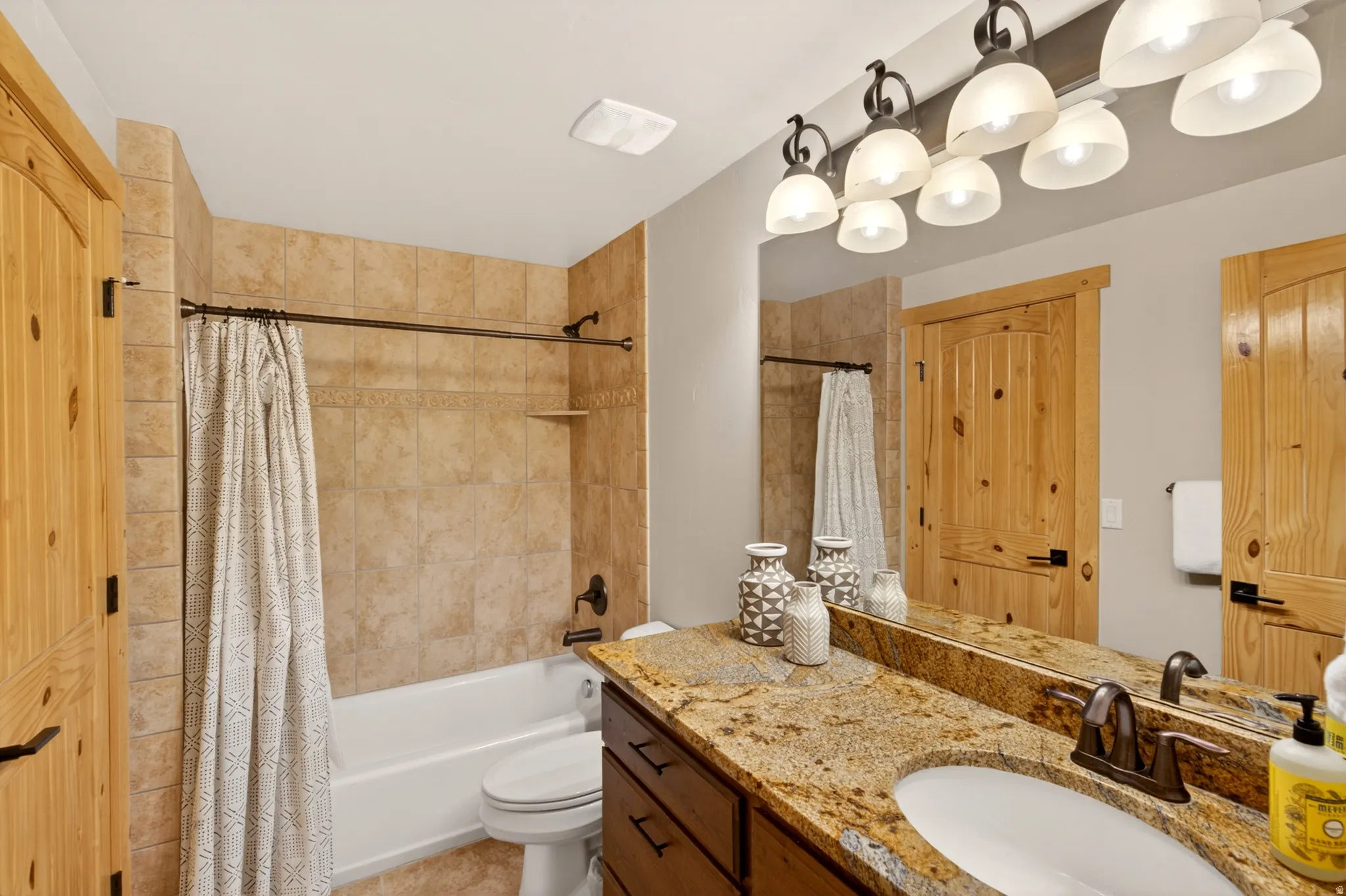 Bathroom featuring a granite-finish countertop, wood-finish cabinetry, drop-in sink with bronze-finish faucet, and a large vanity mirror