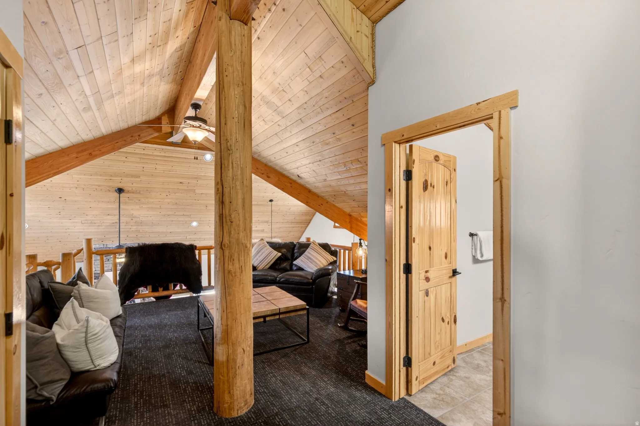 Vaulted wood-paneled ceilings with exposed wood beams, a prominent log column, and wood plank flooring in the loft area