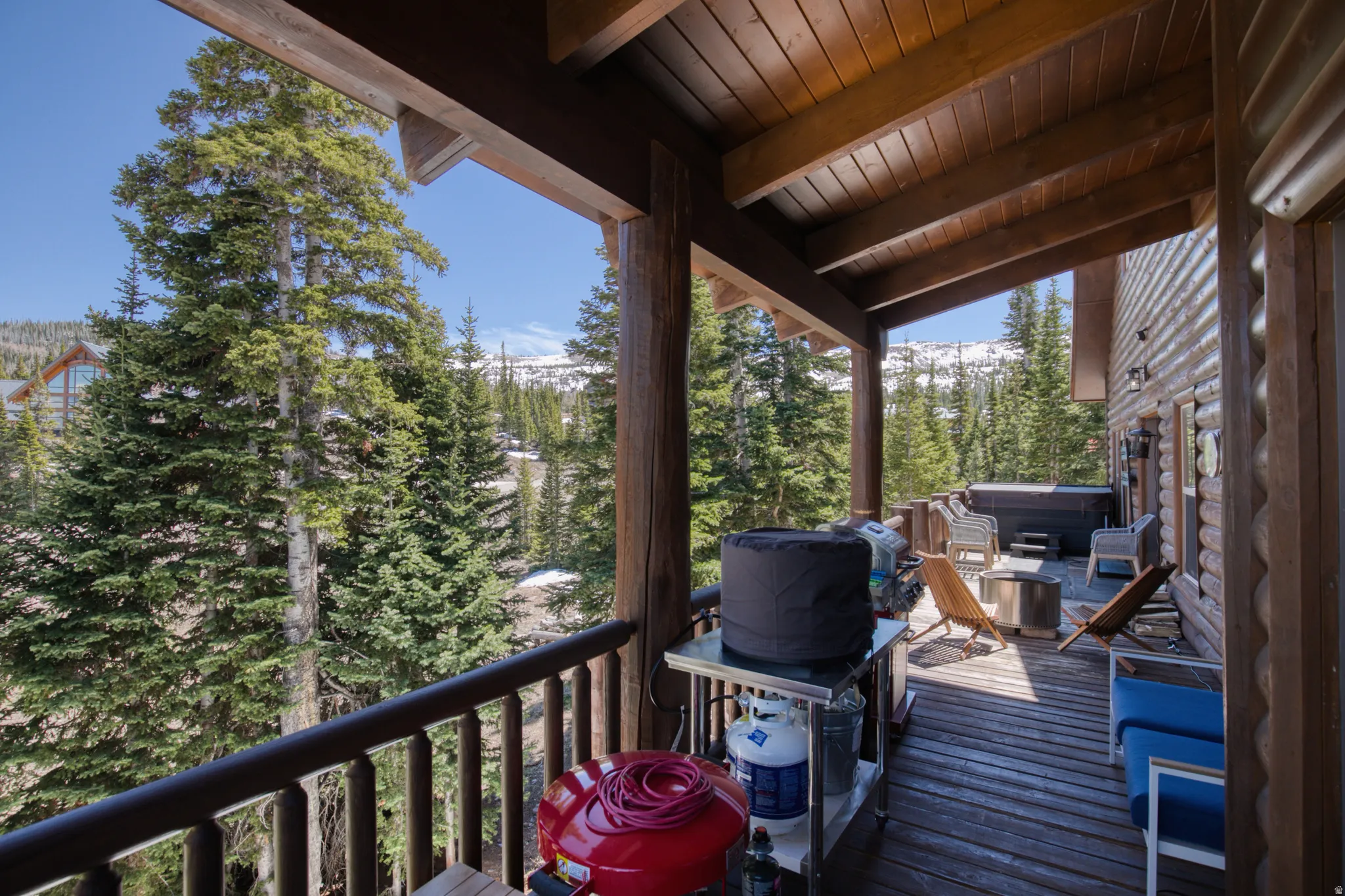 Expansive covered deck featuring a hot tub, log railing, and exposed wood beam ceiling