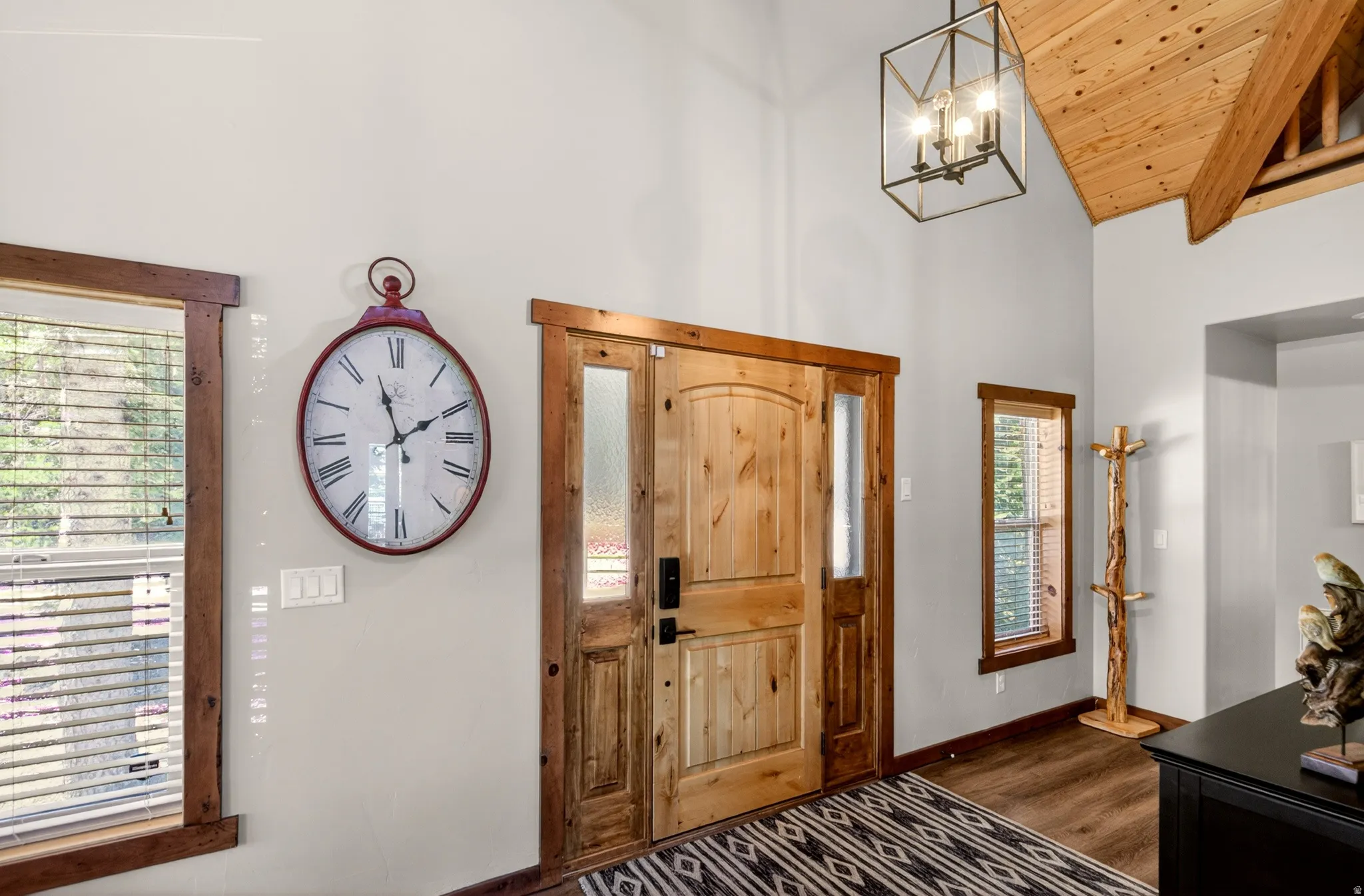 Solid wood entry door with textured glass sidelight, wood-finish flooring, vaulted wood-paneled ceiling with exposed beams, and a modern geometric light fixture