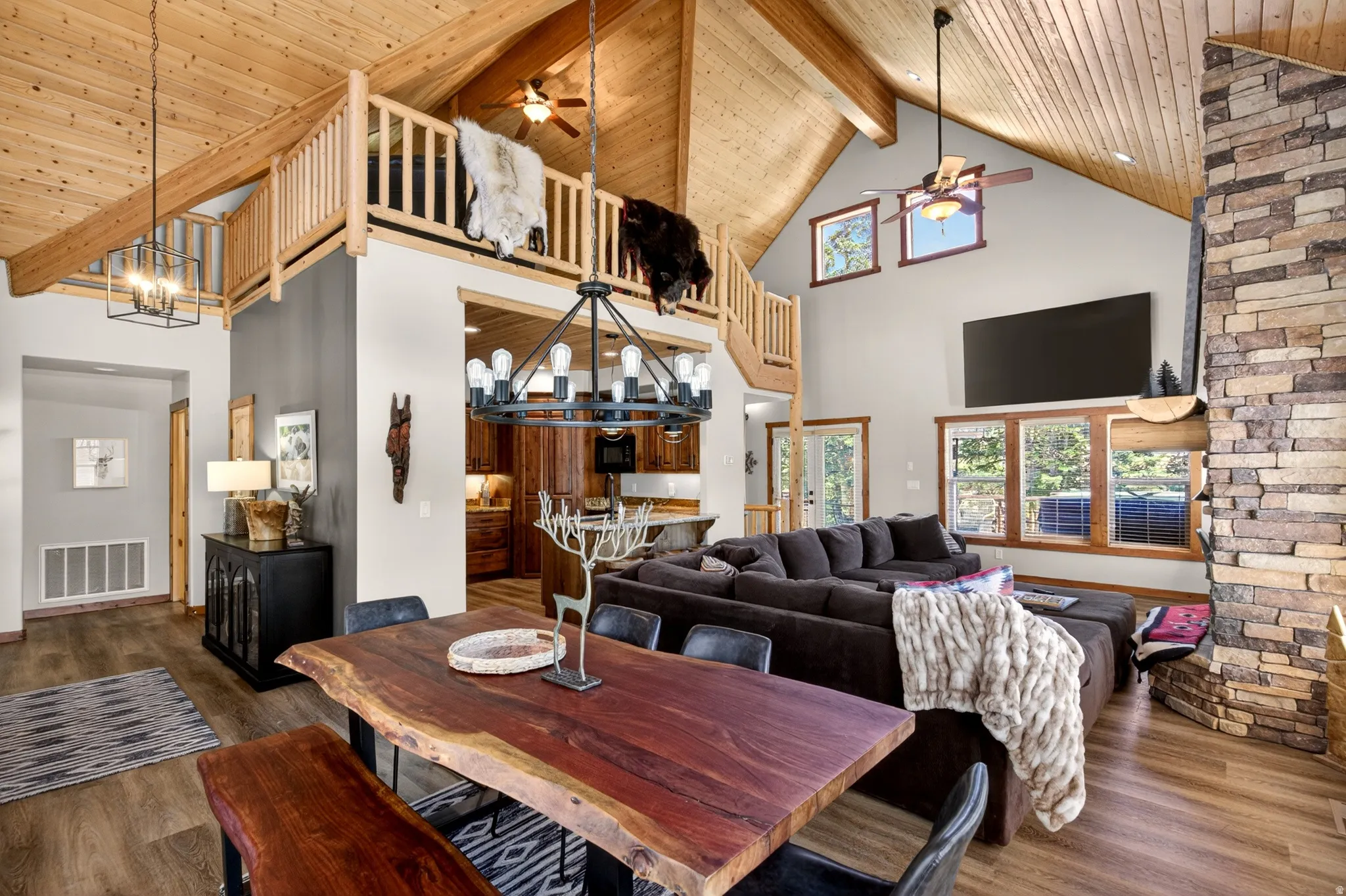 Open-concept living area featuring high vaulted wood-paneled ceilings, a stone fireplace, and wood-finish flooring