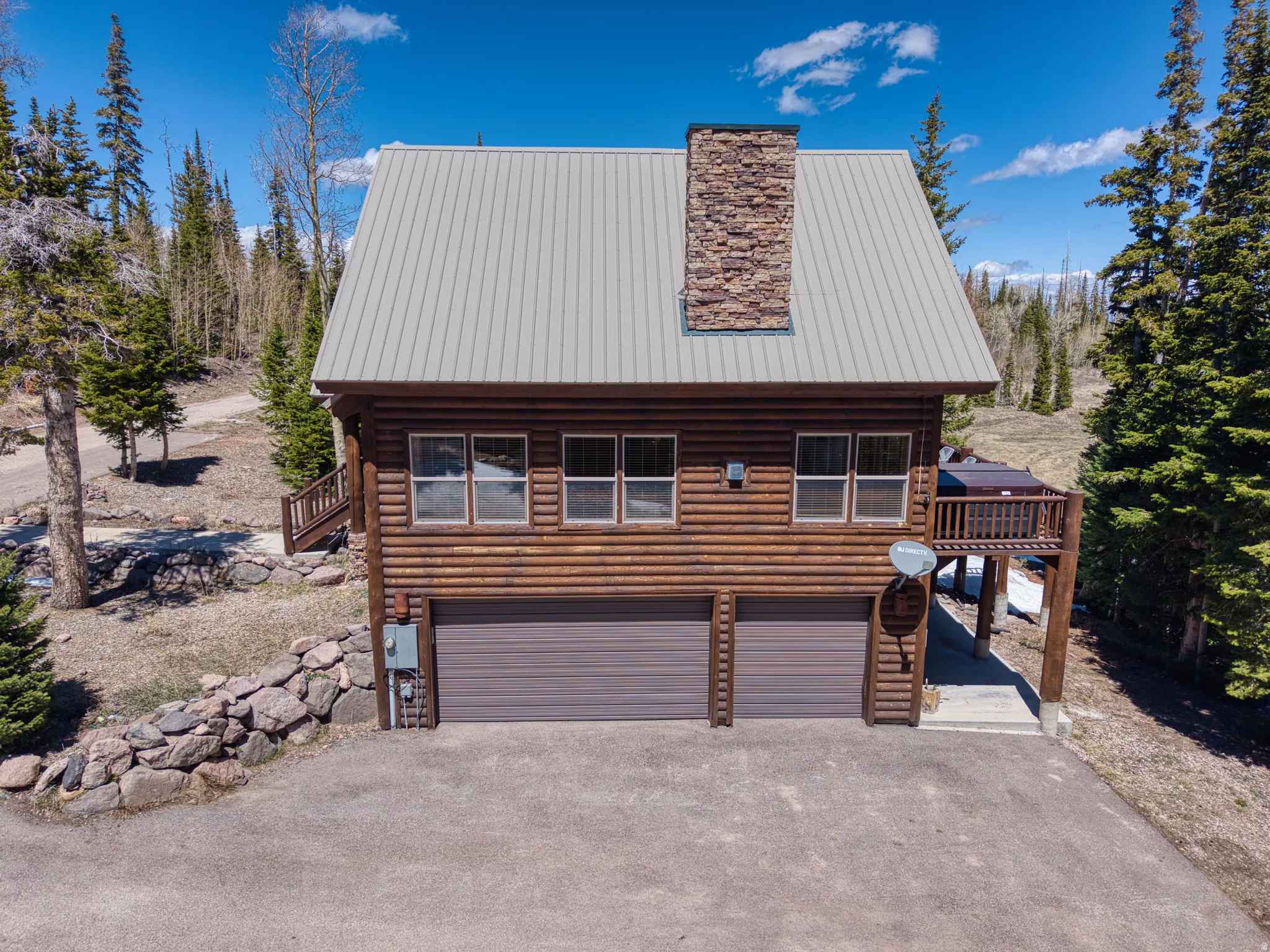 Log cabin exterior featuring a metal roof, stone chimney, and an upper-level deck with an integrated hot tub