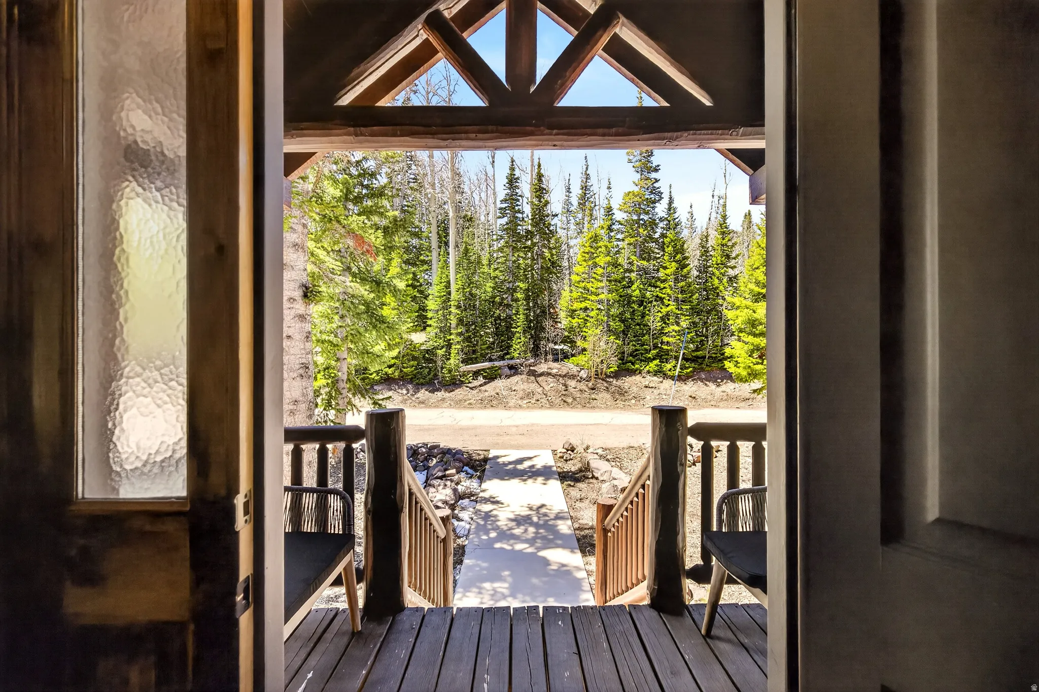 Wood-finish deck with rustic timber railings and structural beams, featuring a glass sidelight and natural tree-lined scenery