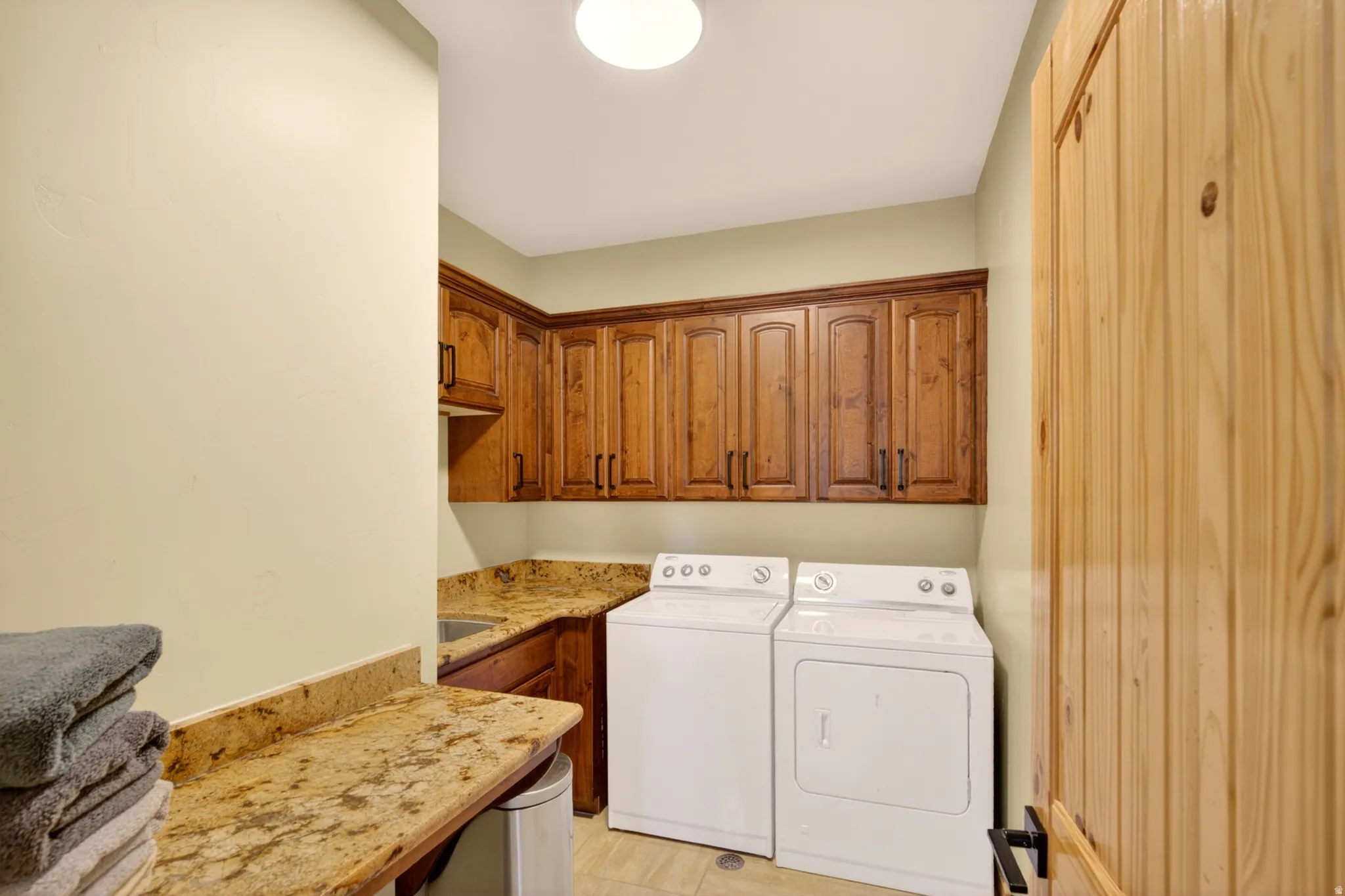 Laundry area featuring wood cabinetry, granite-finish countertops, a built-in sink, and tile flooring