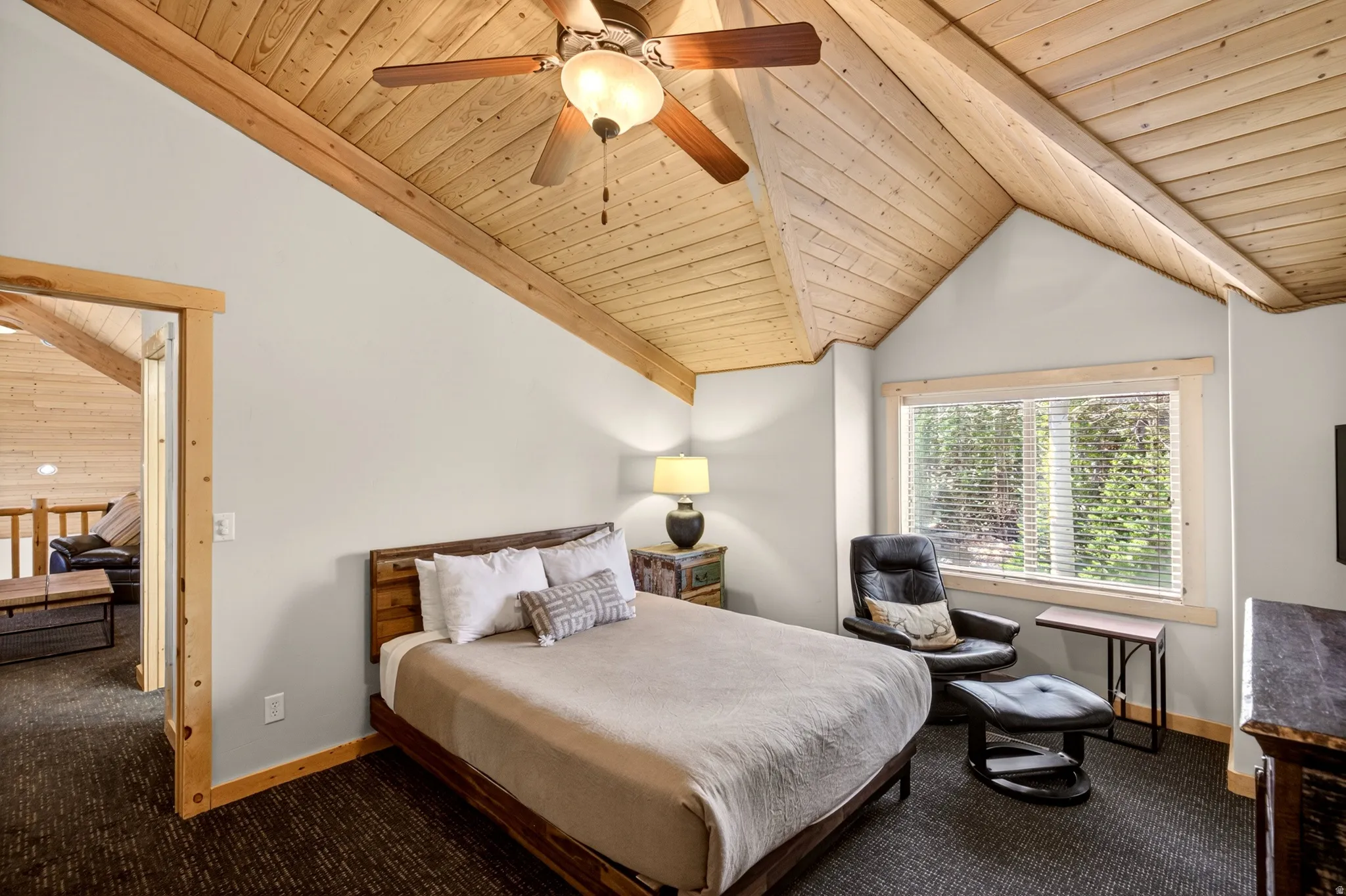 Vaulted wood-paneled ceiling with exposed beams, ceiling fan, carpet flooring, a large window with blinds, and wood trim