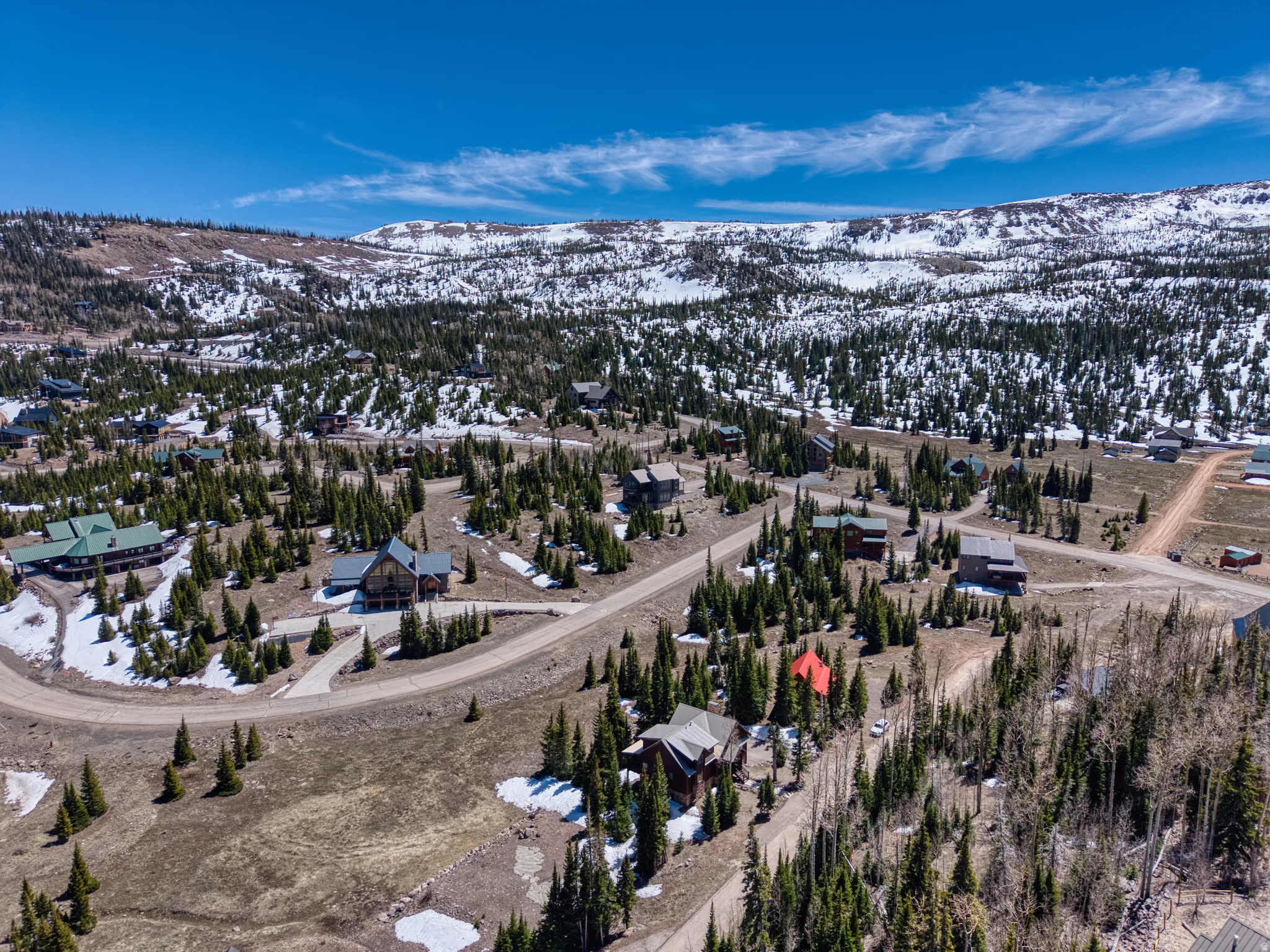Mountainous landscape featuring residential properties, scattered evergreen trees, and visible snow patches
