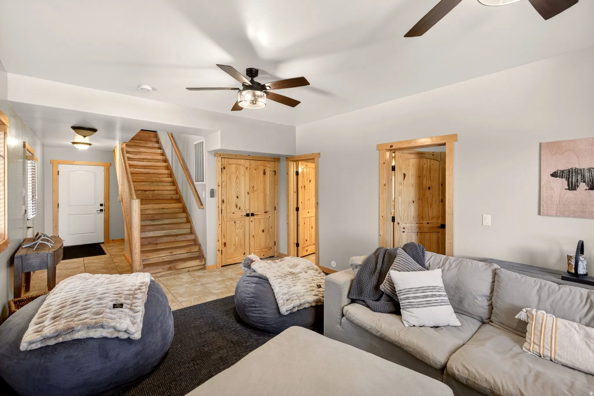 Living area featuring a natural wood staircase, two wood-paneled doors with black hardware, and light-toned tile flooring at the entry