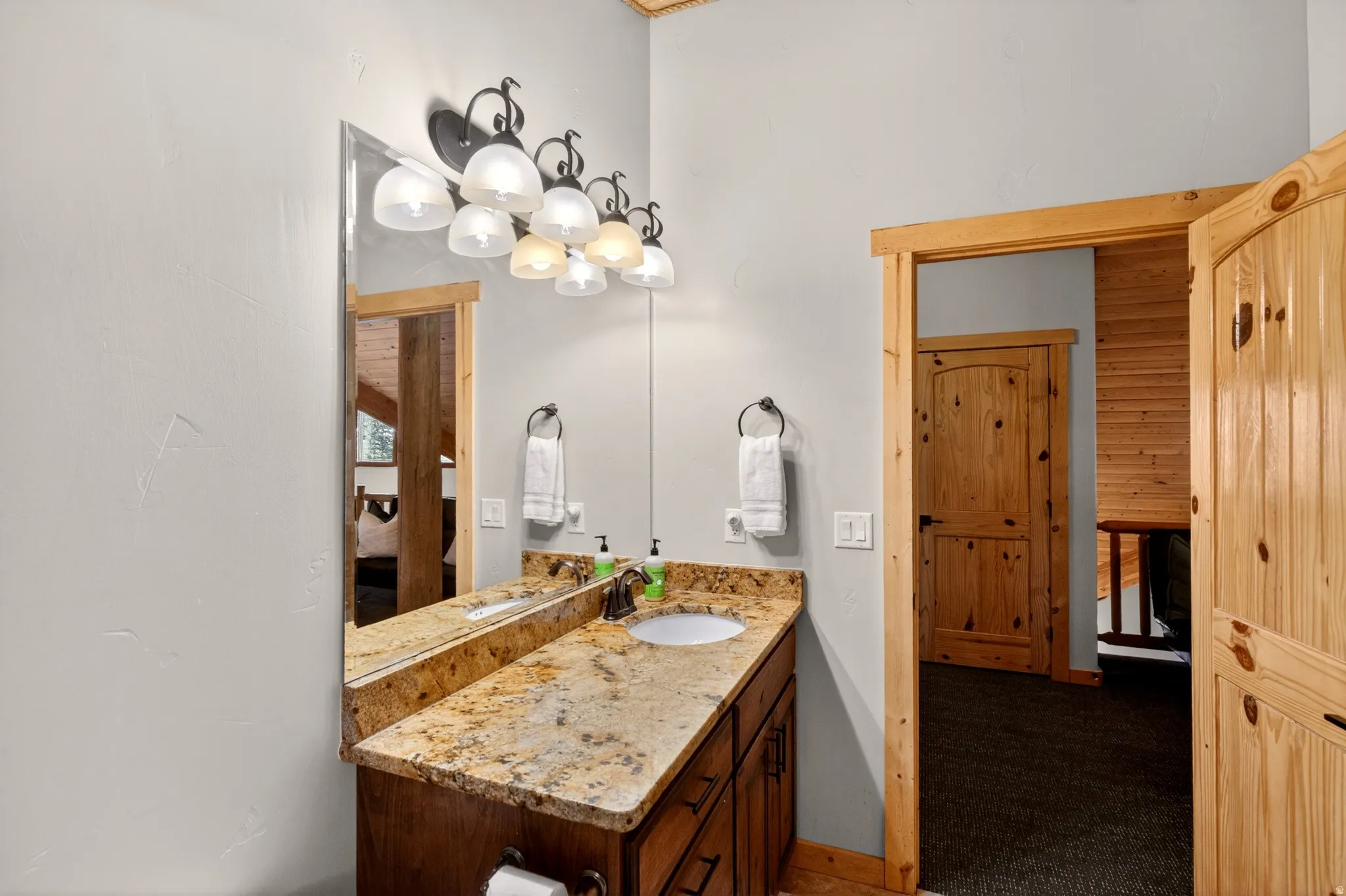 Bathroom vanity featuring a polished stone countertop with an undermount sink, dark wood cabinetry, and a wall-mounted mirror