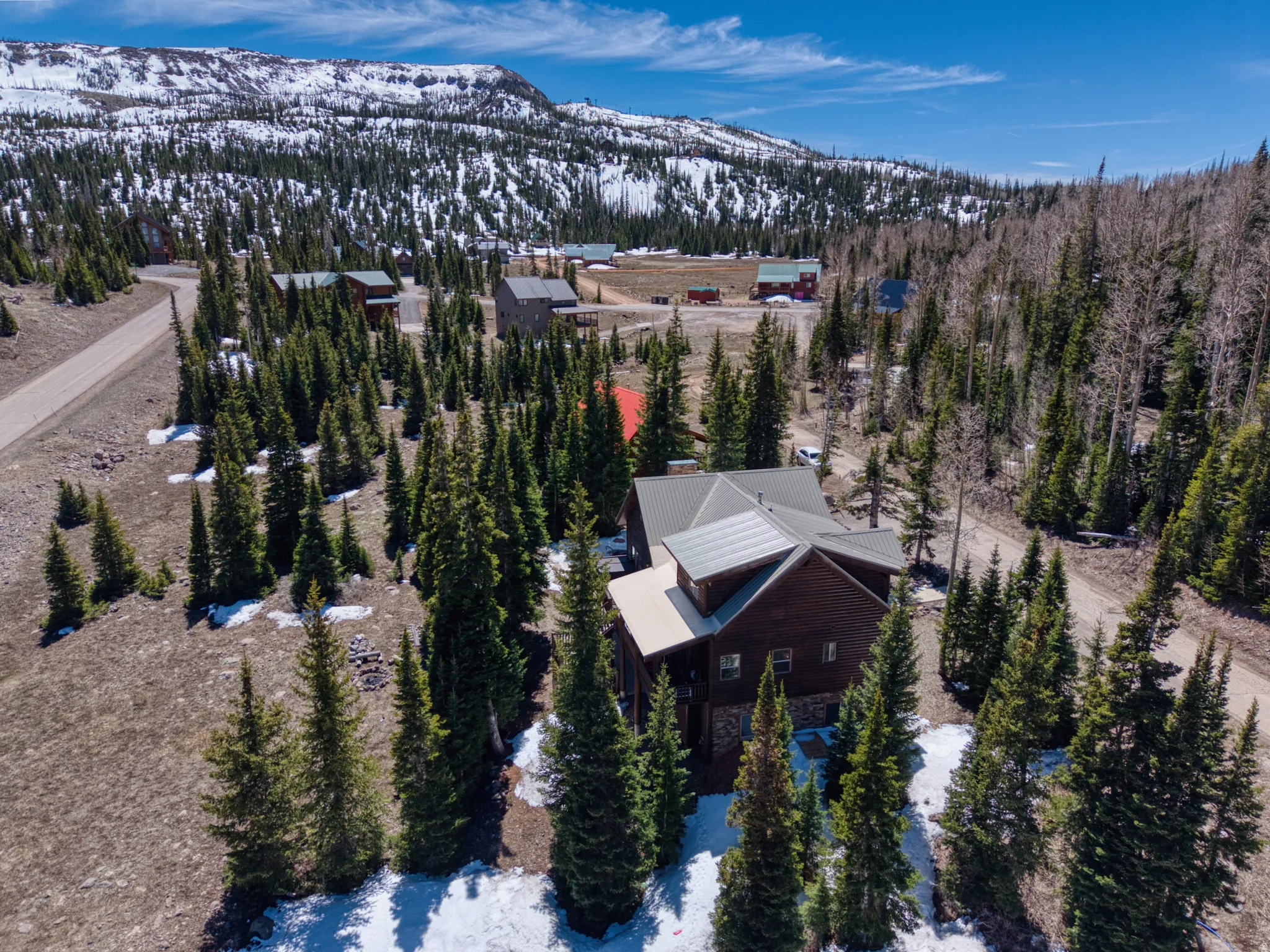Mountain property featuring a multi-level structure with a metal roof, surrounded by numerous evergreen trees