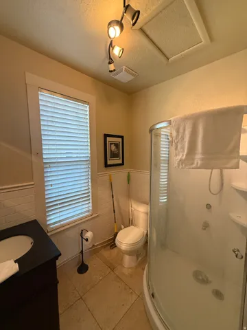 Bathroom featuring a curved glass shower enclosure, white subway tile wainscoting, a dark wood-finish vanity with an integrated sink, a window with blinds, and tile flooring