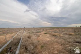 Expansive open land featuring a visible irrigation system and distant natural foliage