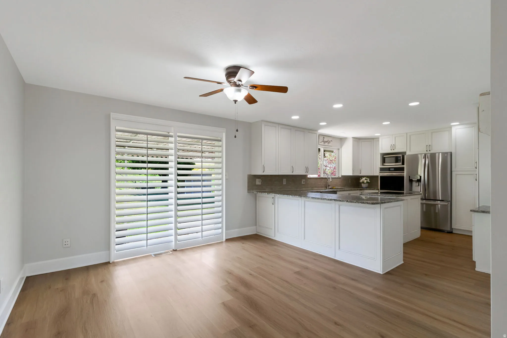 Open-concept living area featuring wood-look flooring, a contemporary ceiling fan, and sliding glass doors with white plantation shutters