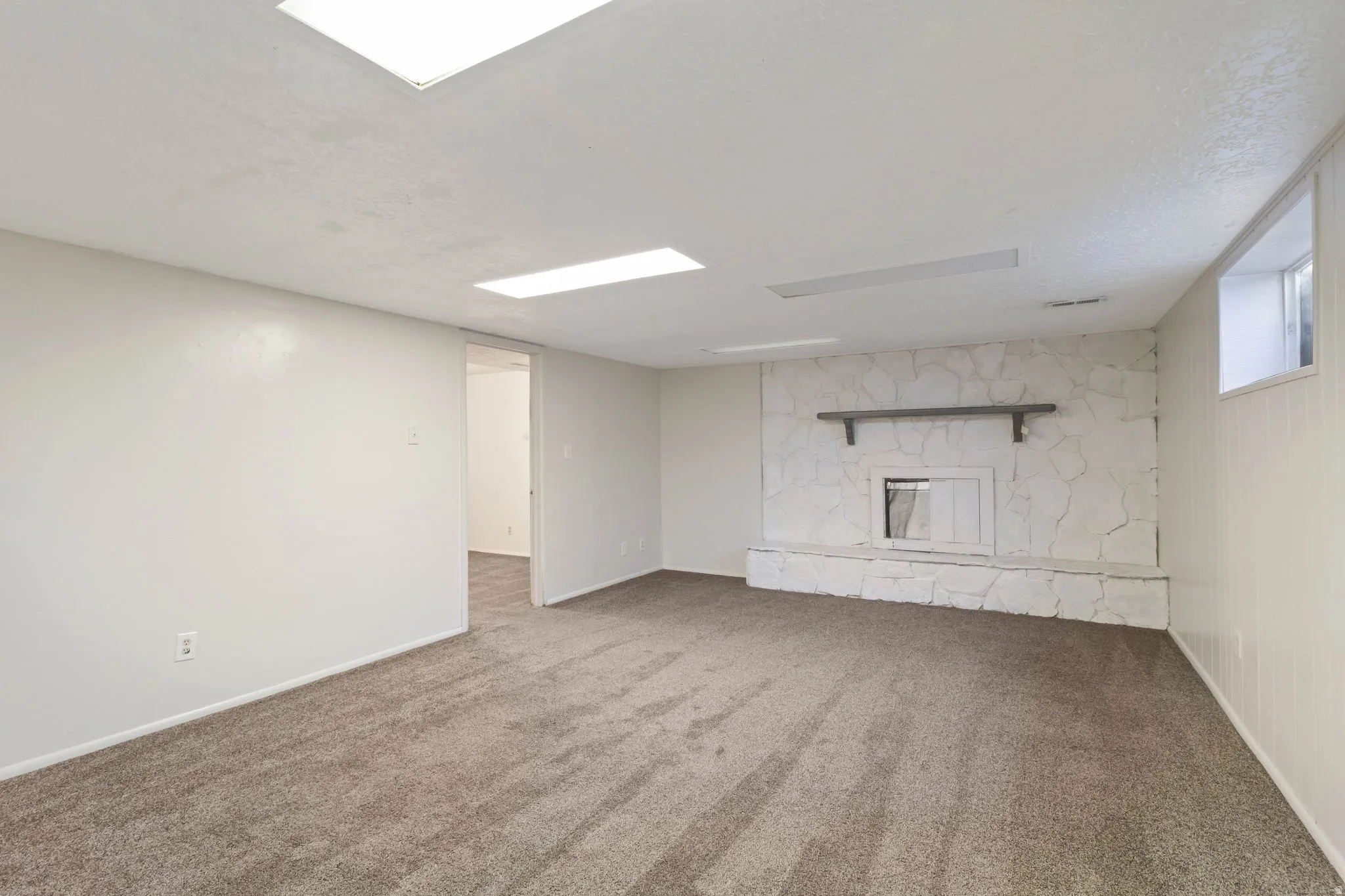 Spacious room featuring a stone-clad fireplace with a mantel, carpeted flooring, white walls, and recessed lighting