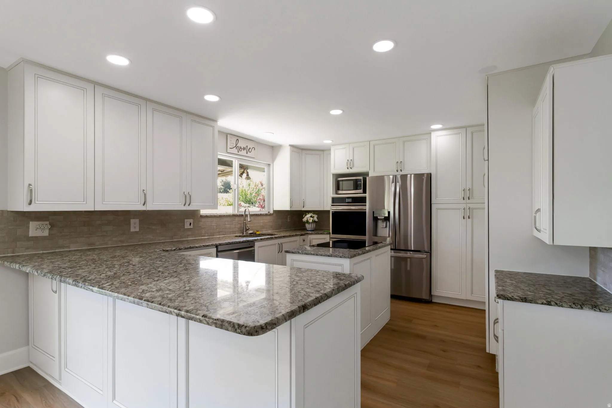 Kitchen featuring white cabinetry with brushed nickel hardware, granite countertops, stainless steel appliances, a tile backsplash, and wood-look flooring