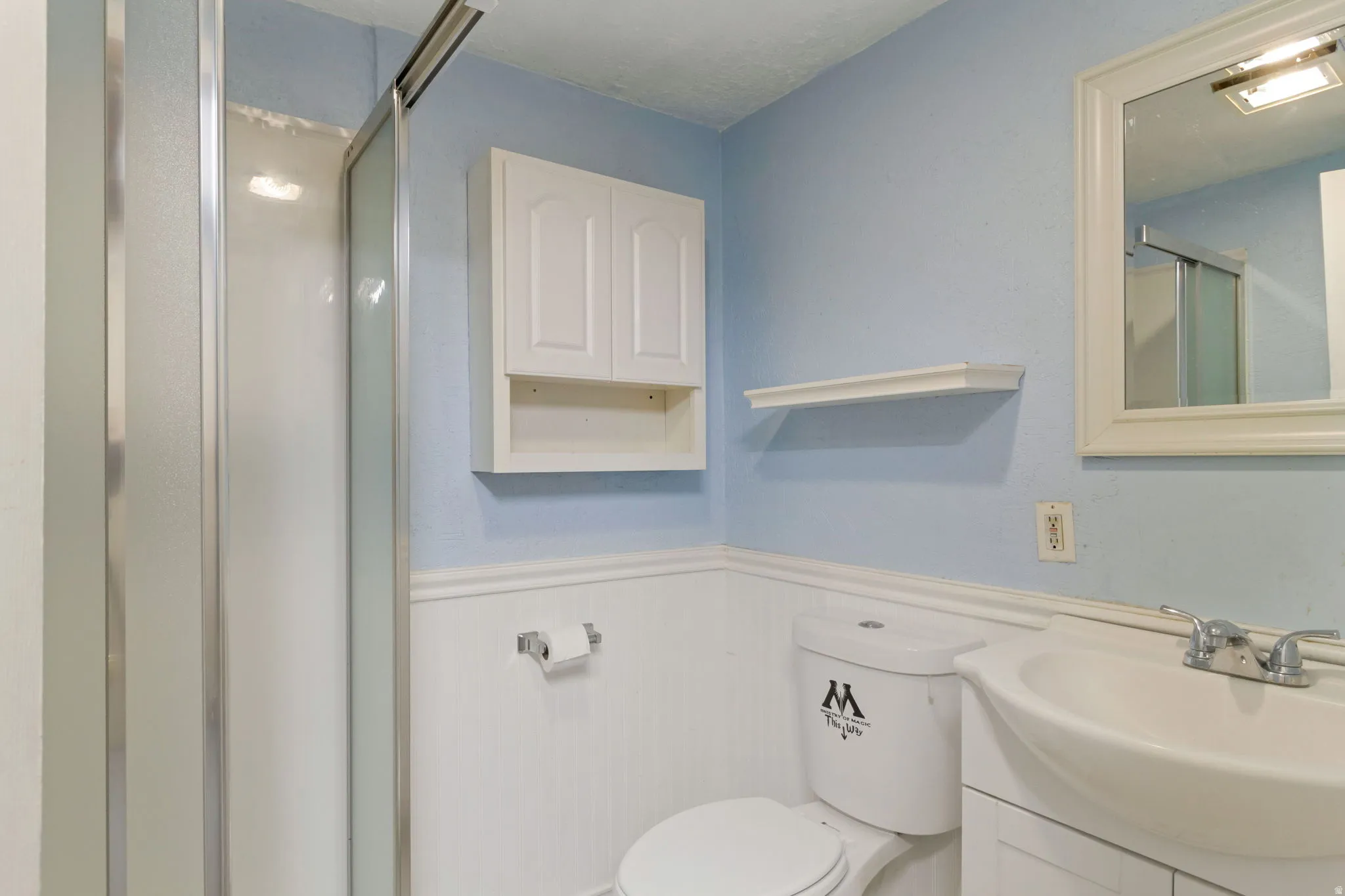Bathroom featuring a glass-enclosed shower, wall-mounted storage cabinet, white vanity with integrated sink, and framed mirror
