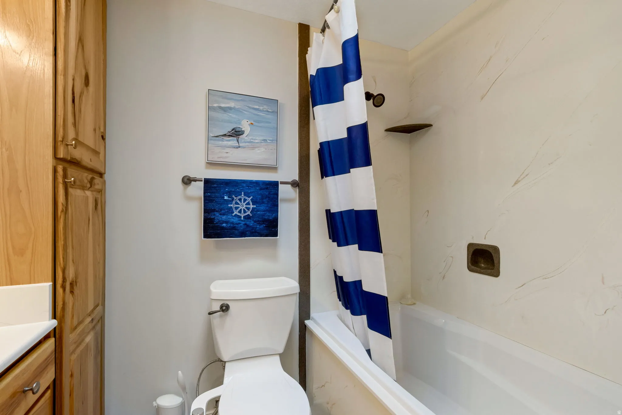 Full bathroom featuring a white bathtub/shower combination with a single shower head, a standard white toilet, and light wood-finish cabinetry