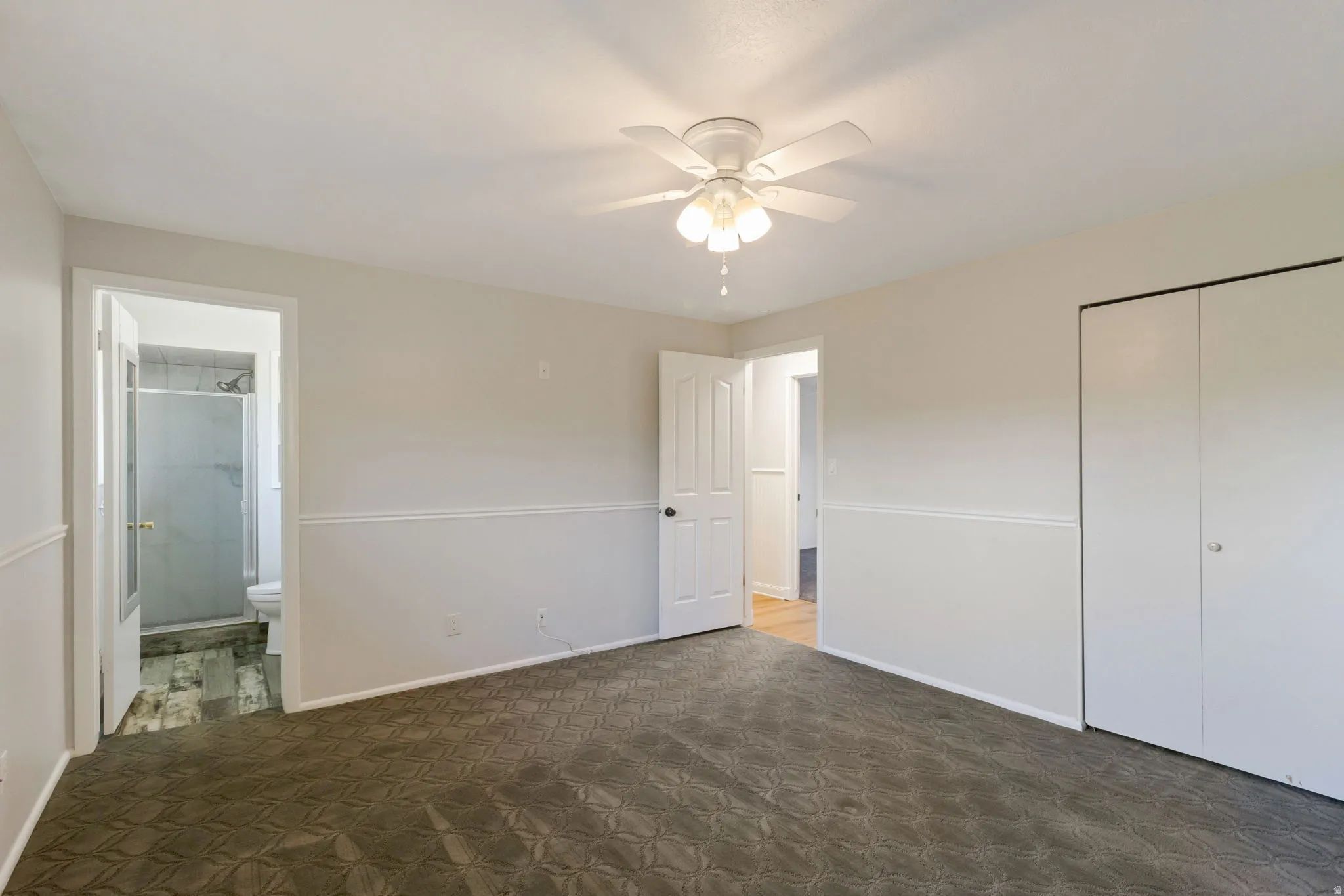 Carpeted bedroom featuring a ceiling fan with light fixture, chair rail molding, and panel doors