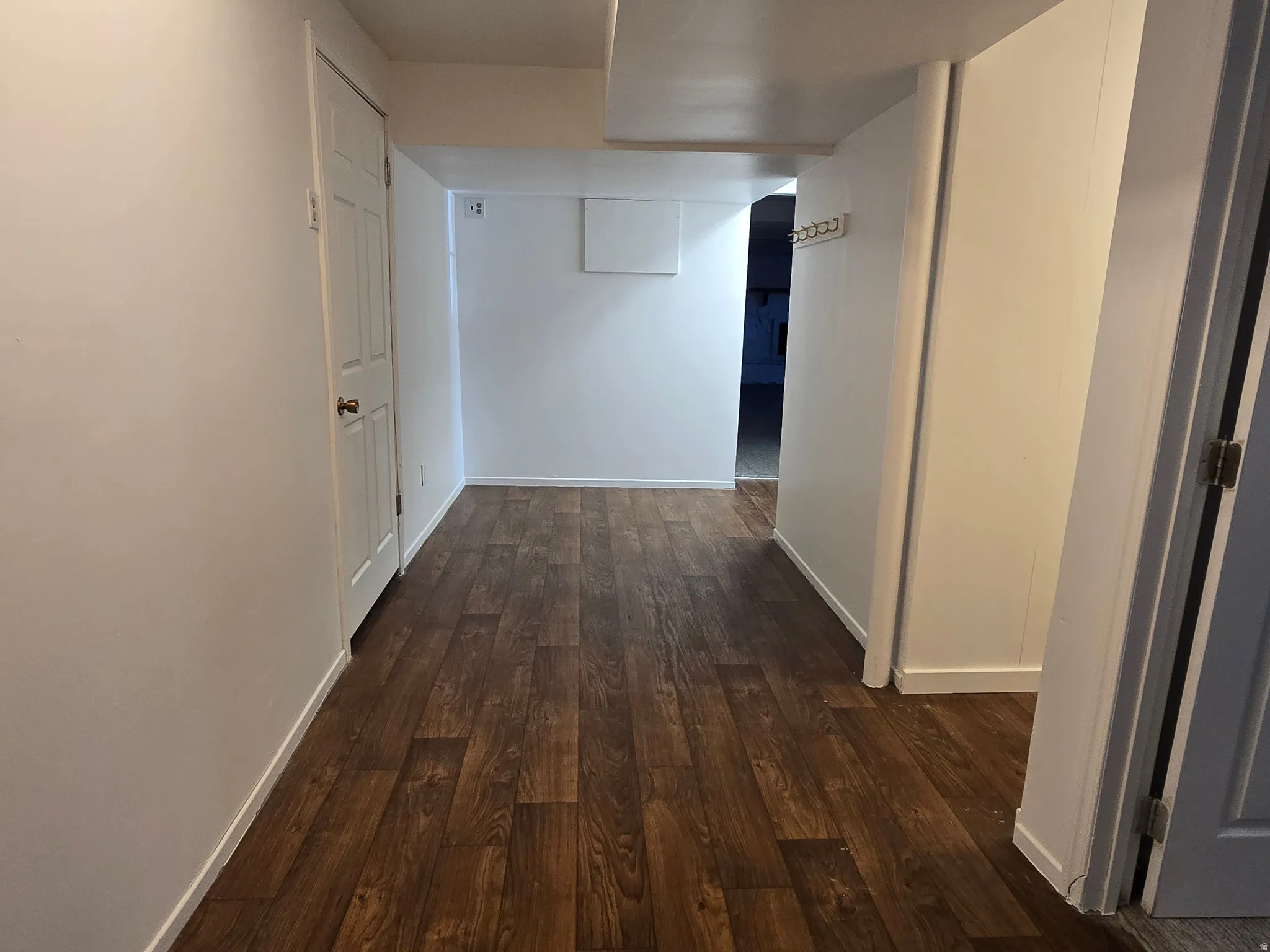 Spacious hallway flooring showcasing warm wood-finish planks throughout, complemented by clean white walls and multiple doorways providing access to adjoining rooms