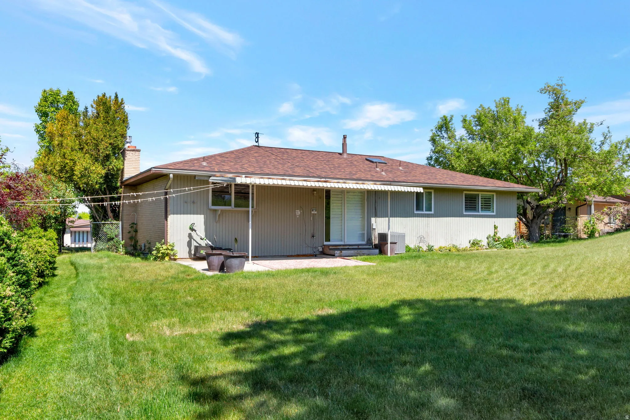 Expansive backyard with a flat lawn, mature perimeter trees, patio area, and a covered awning